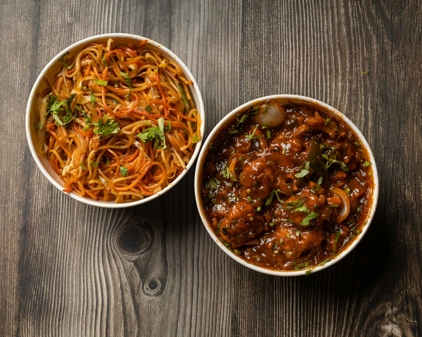 Vibrant bowls of Indo-Chinese noodles and Manchurian on a rustic wooden surface. - healthy dinner for two