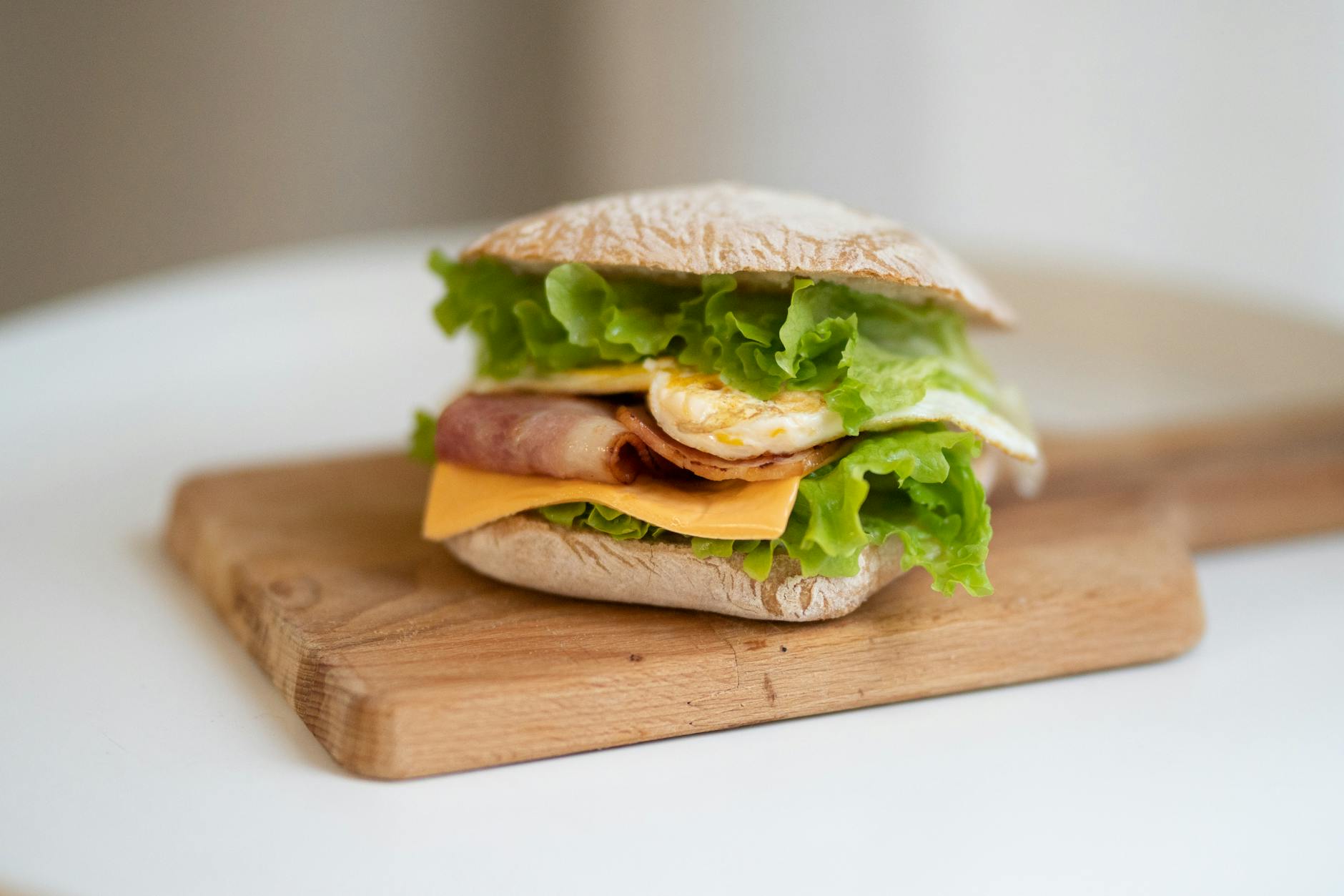Delicious sandwich with bacon, lettuce, cheese, and egg on a wooden board. - healthy fast food breakfast