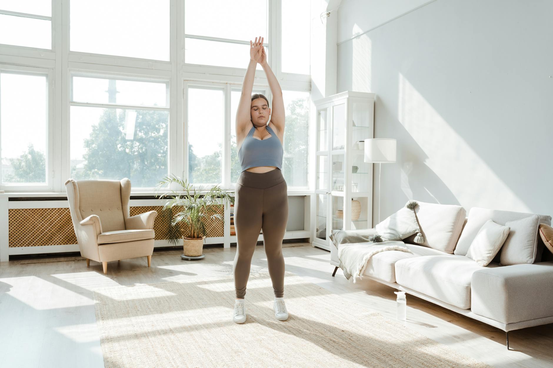 A woman practices stretching exercises in a sunlit living room, promoting wellness and healthy lifestyle. - healthy morning habits
