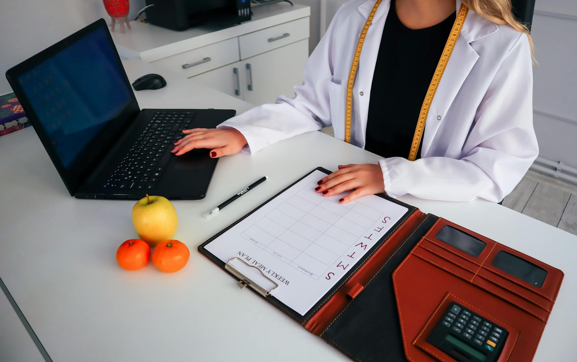 Dietitian working on meal plan with laptop, fruits, and calendar for health consultation. - healthy office snacks