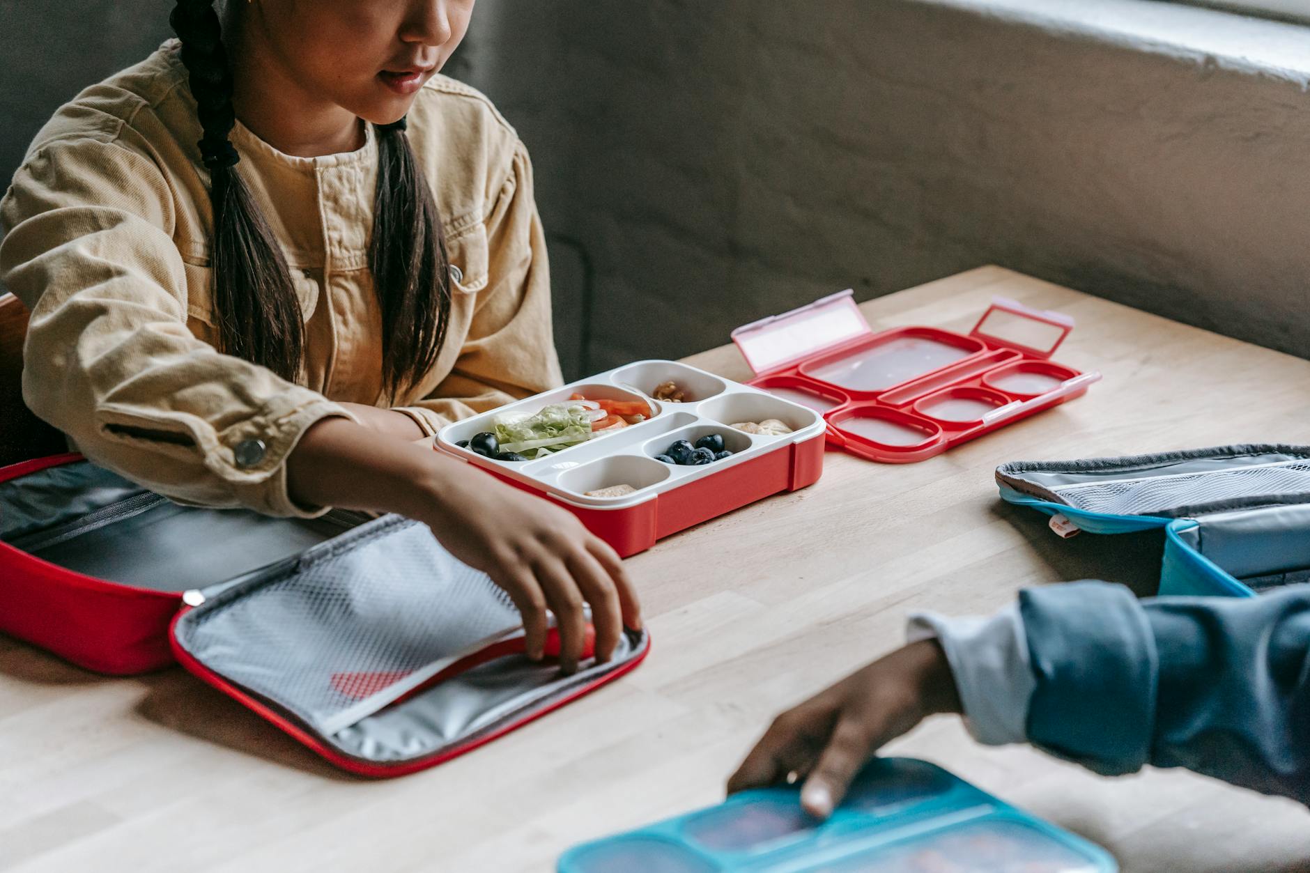 From above of crop anonymous ethnic schoolkids with lunch boxes full of delicious food in classroom - healthy school lunches