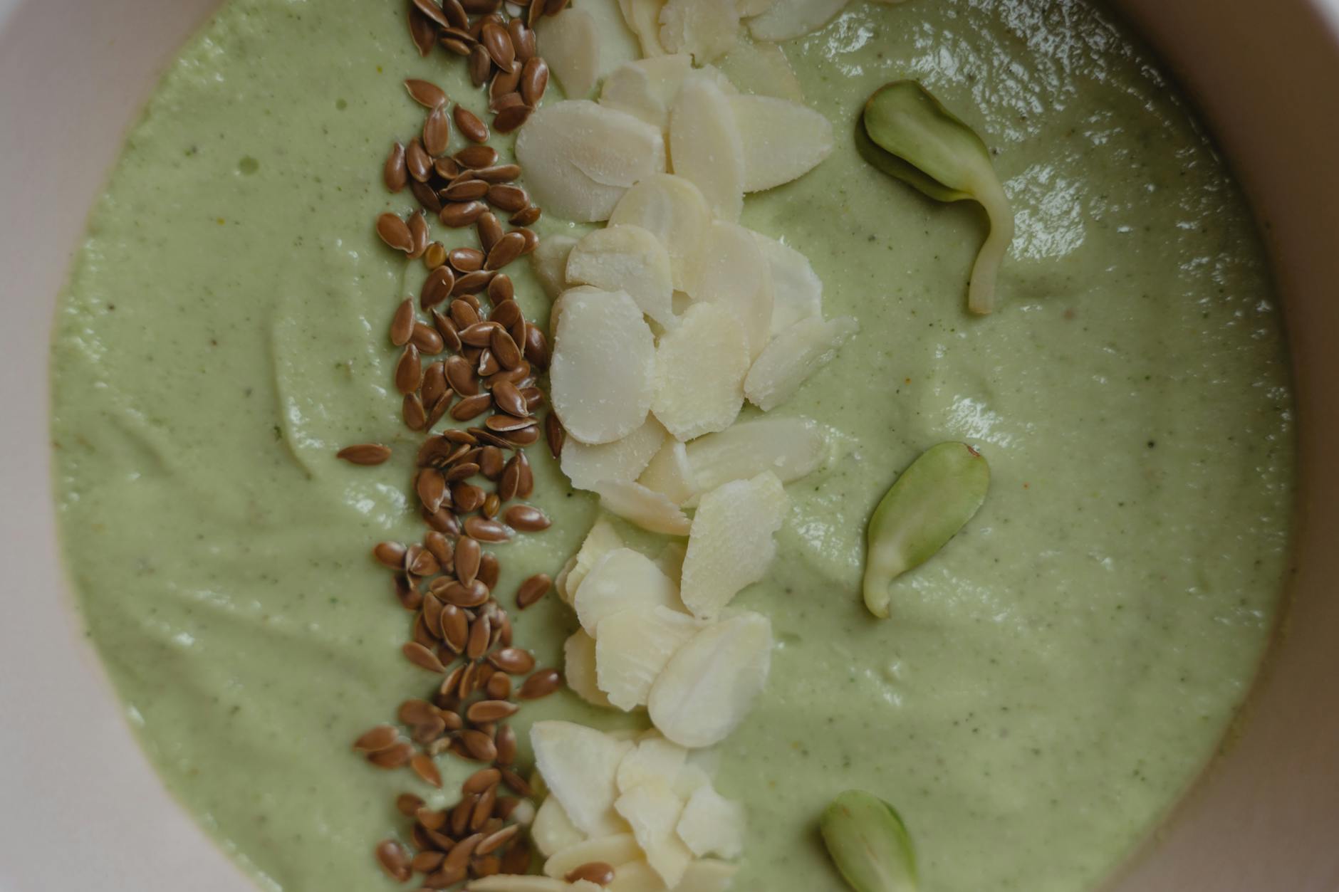 A vibrant green smoothie bowl garnished with flax seeds, almonds, and pumpkin seeds. - healthy smoothie recipe