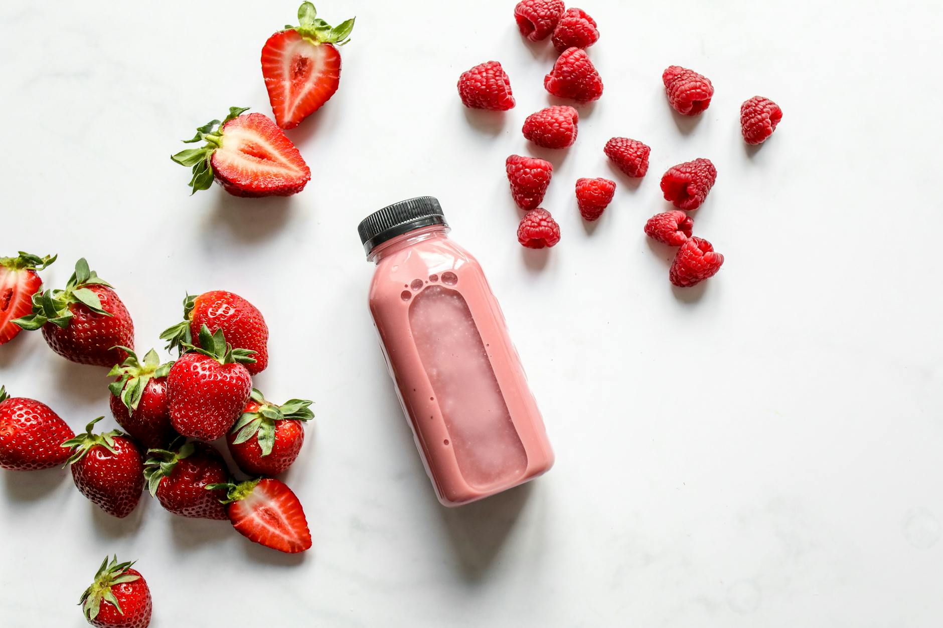 Top view of fresh strawberry and raspberry smoothie in a bottle with scattered fruits on white background. - healthy smoothie recipe