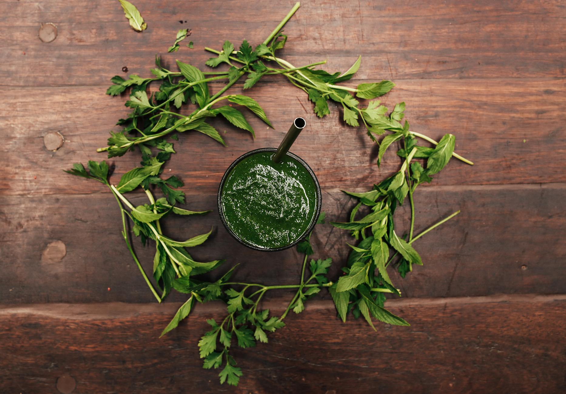 Top view of a green smoothie in a glass surrounded by fresh herbs on a wooden table. - healthy smoothies