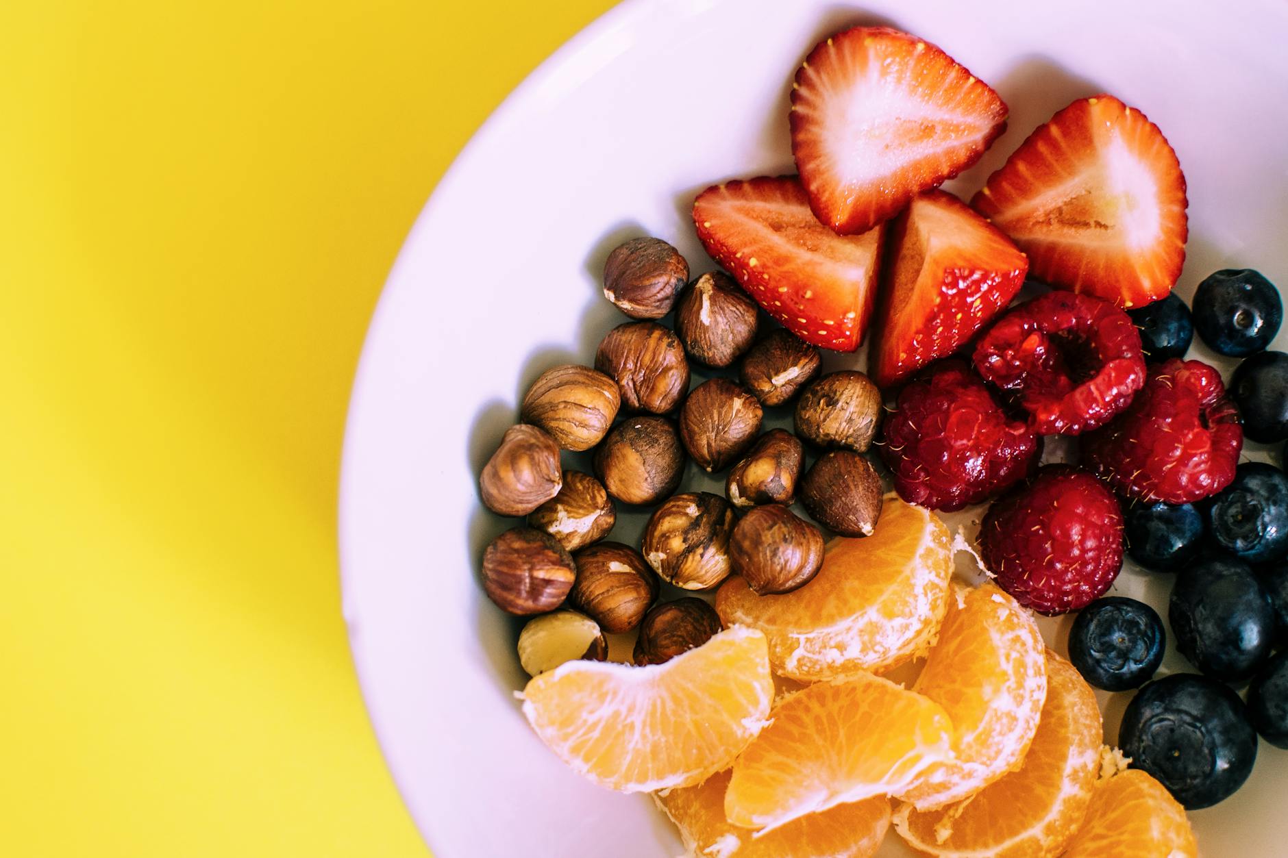 Close-up of a bowl with fresh fruits and nuts against a vibrant yellow backdrop. - healthy snacks walmart