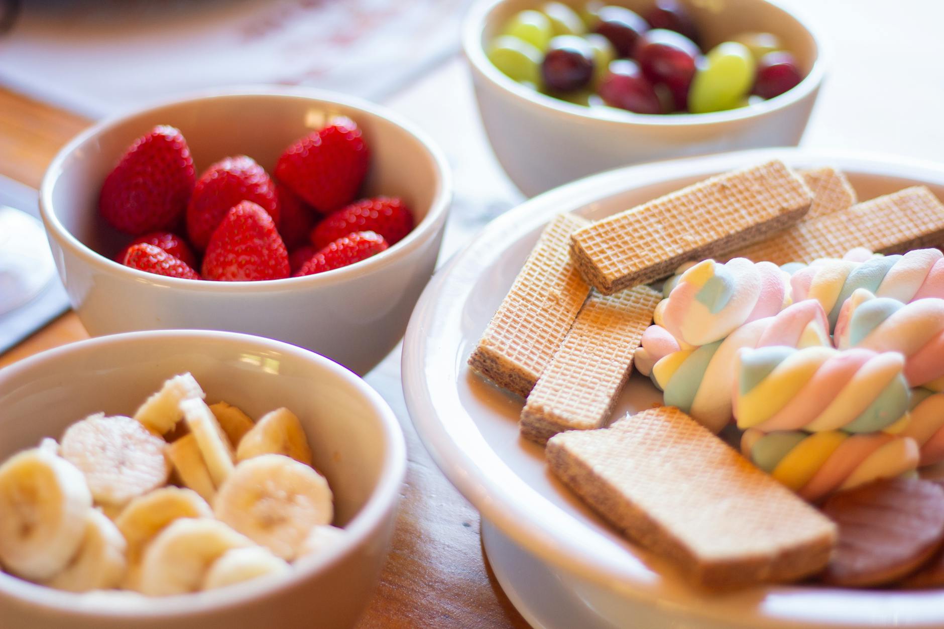 Colorful display of fruits and sweets including strawberries, bananas, grapes, wafers, and marshmallows. - healthy sweet snacks