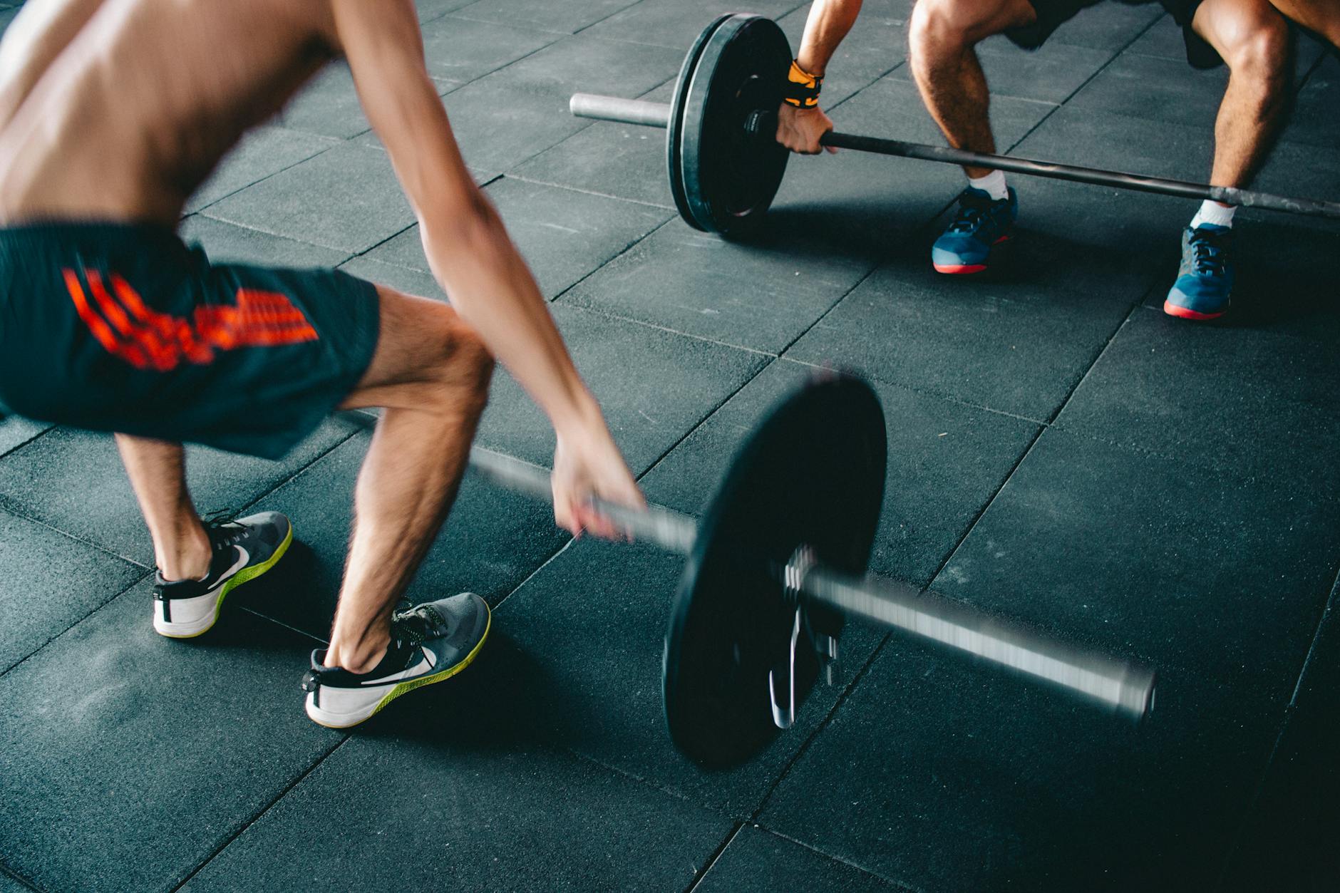 Two men lifting barbells showing strength and effort in a gym setting. - high intensity interval training
