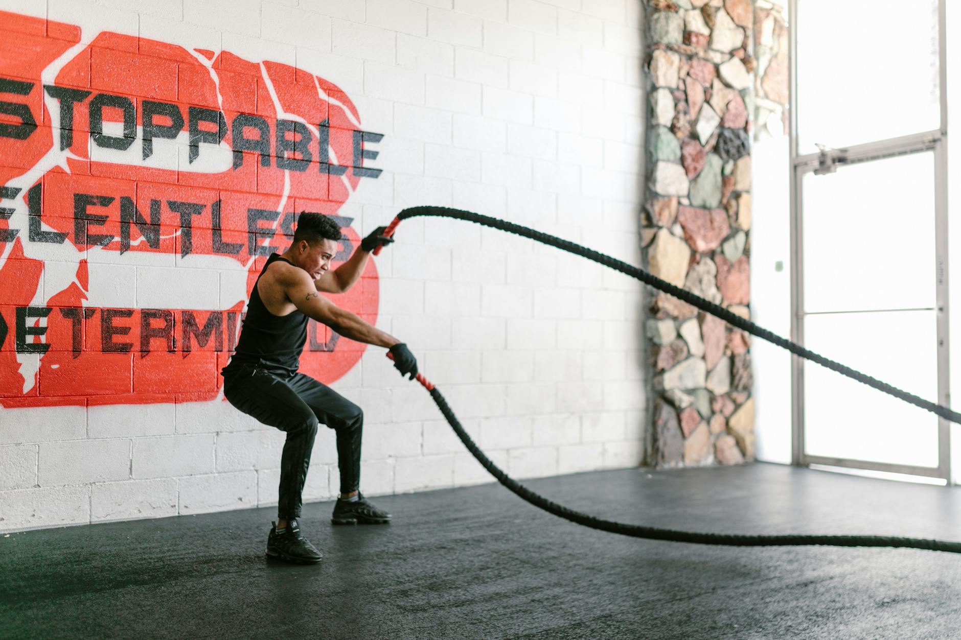 Athletic man training with battle ropes in a gym with motivational wall art. - what is hiit