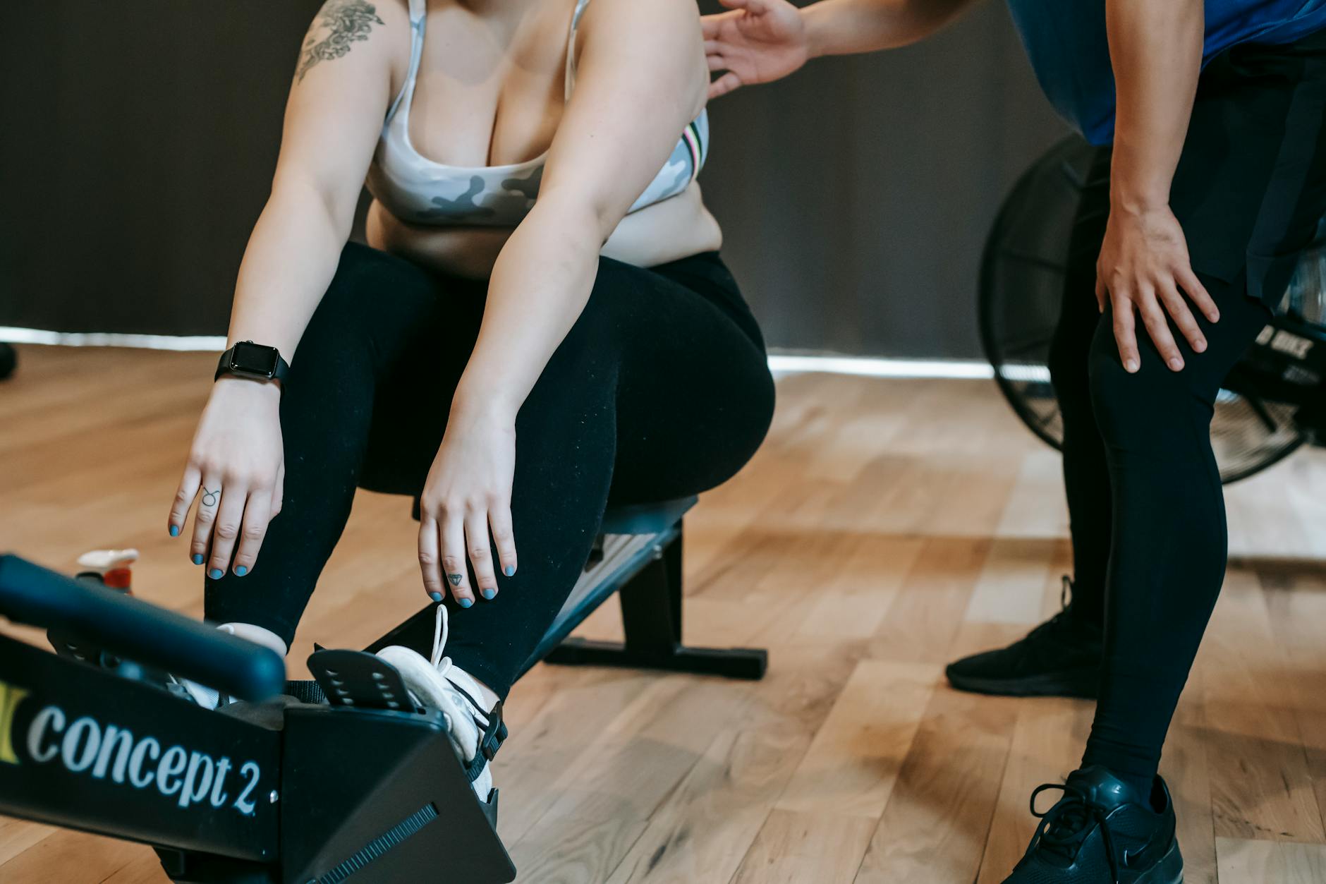 Focused gym session featuring a woman on a rowing machine receiving guidance from a trainer. - hiit fat loss