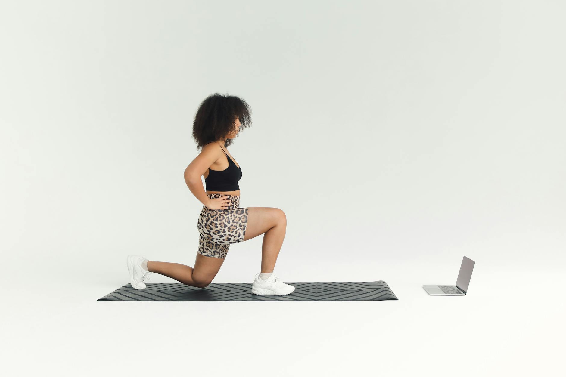 A woman doing a lunge exercise indoors with a laptop for guidance. - home cardio workout