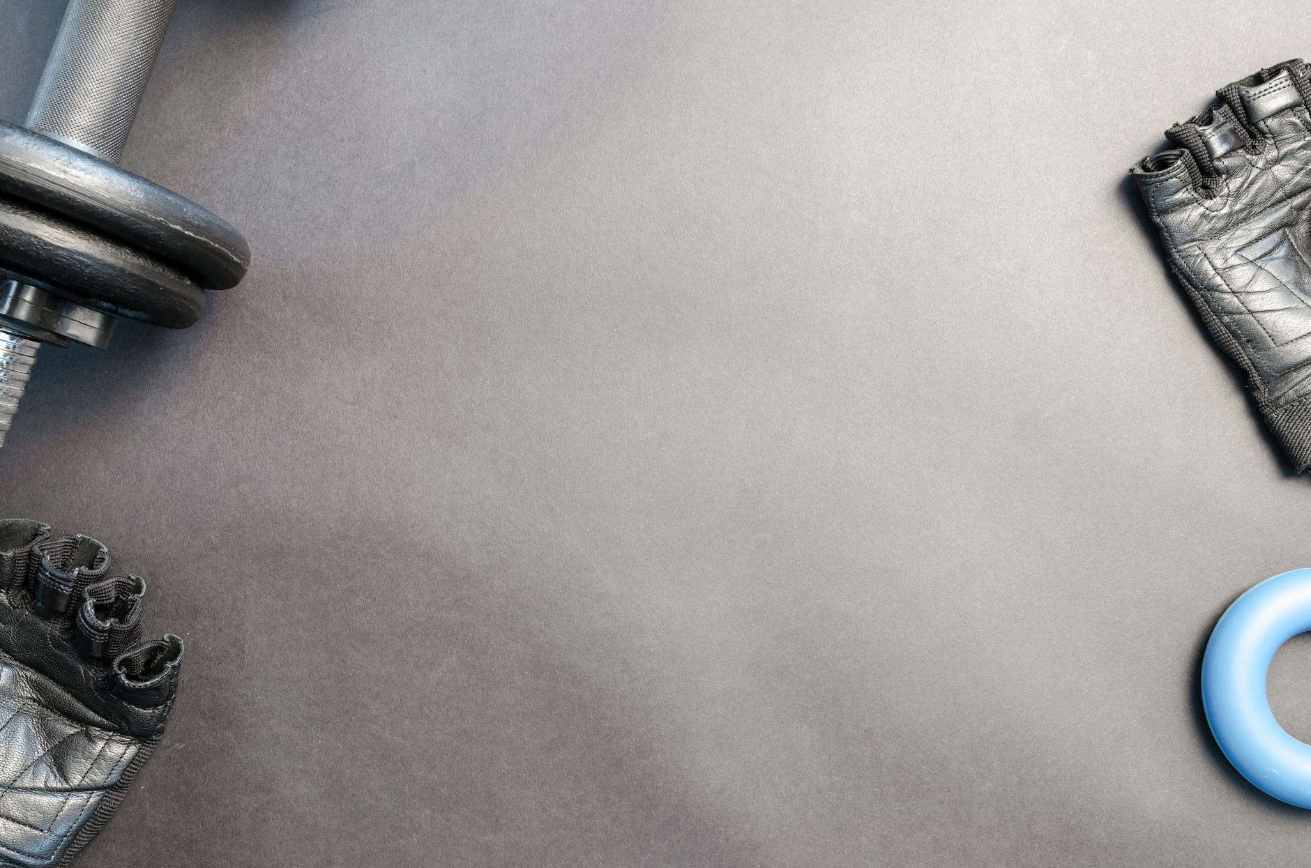 A flat lay of gym essentials including a dumbbell, gloves, and a fitness ring on a neutral background. - home workout plan