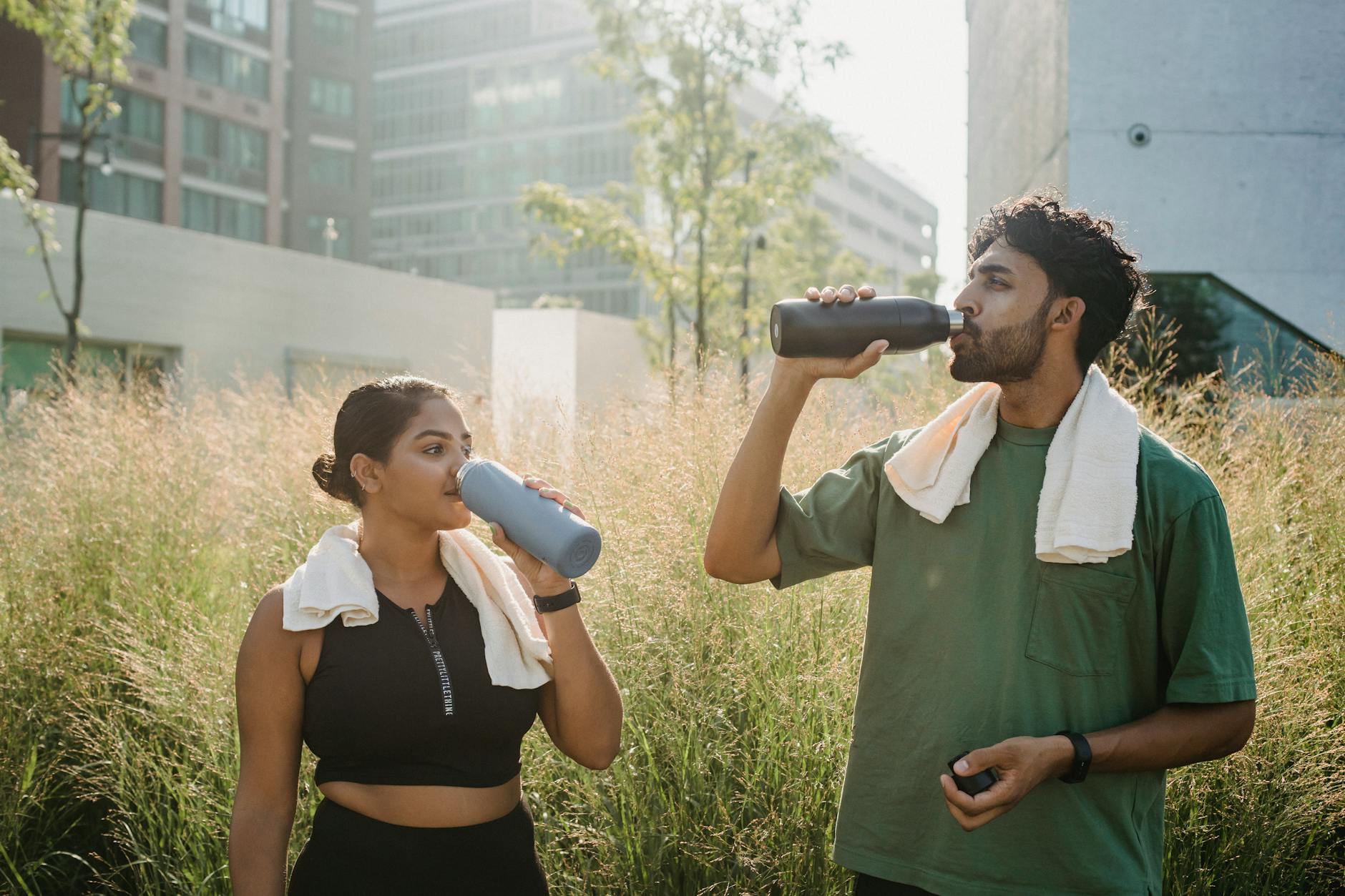 A man and woman take a refreshing break, drinking water after exercising in an urban park. - hydration hacks