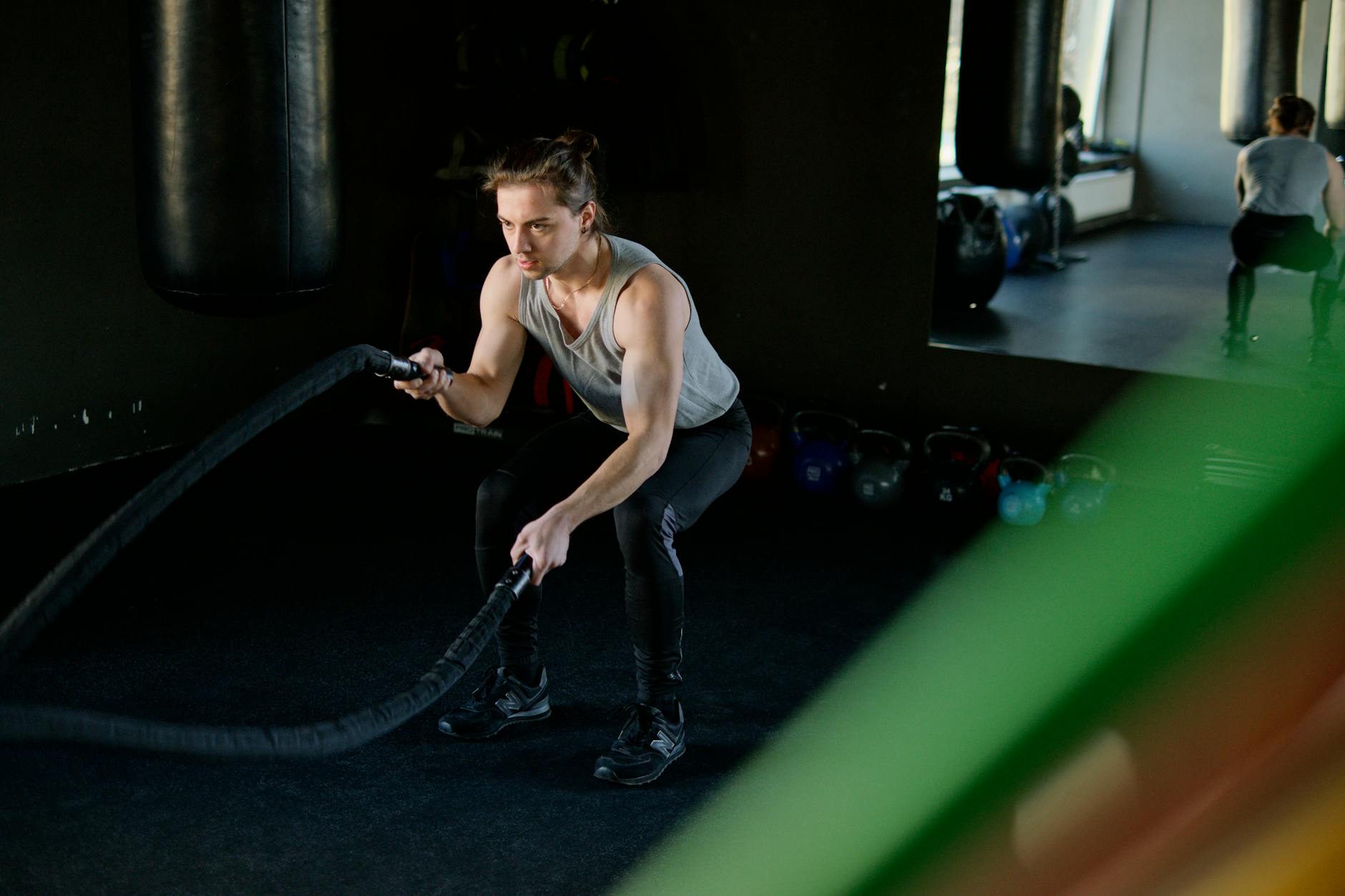 Man engages in an intense battle rope workout in a gym, focusing on fitness and strength. - interval training workouts