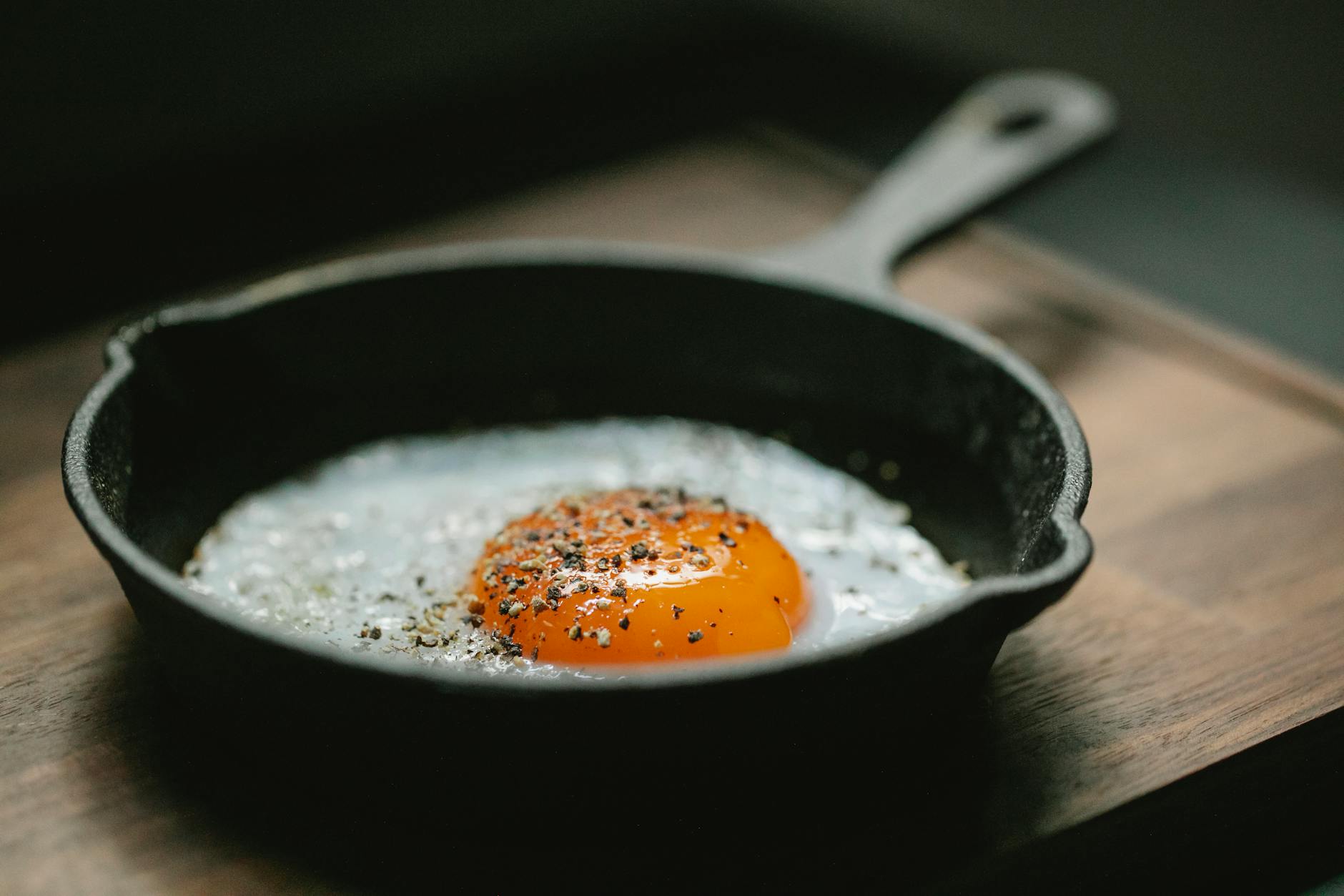 High angle of pan with fried egg with seasoning placed on wooden board in kitchen - iron protein foods