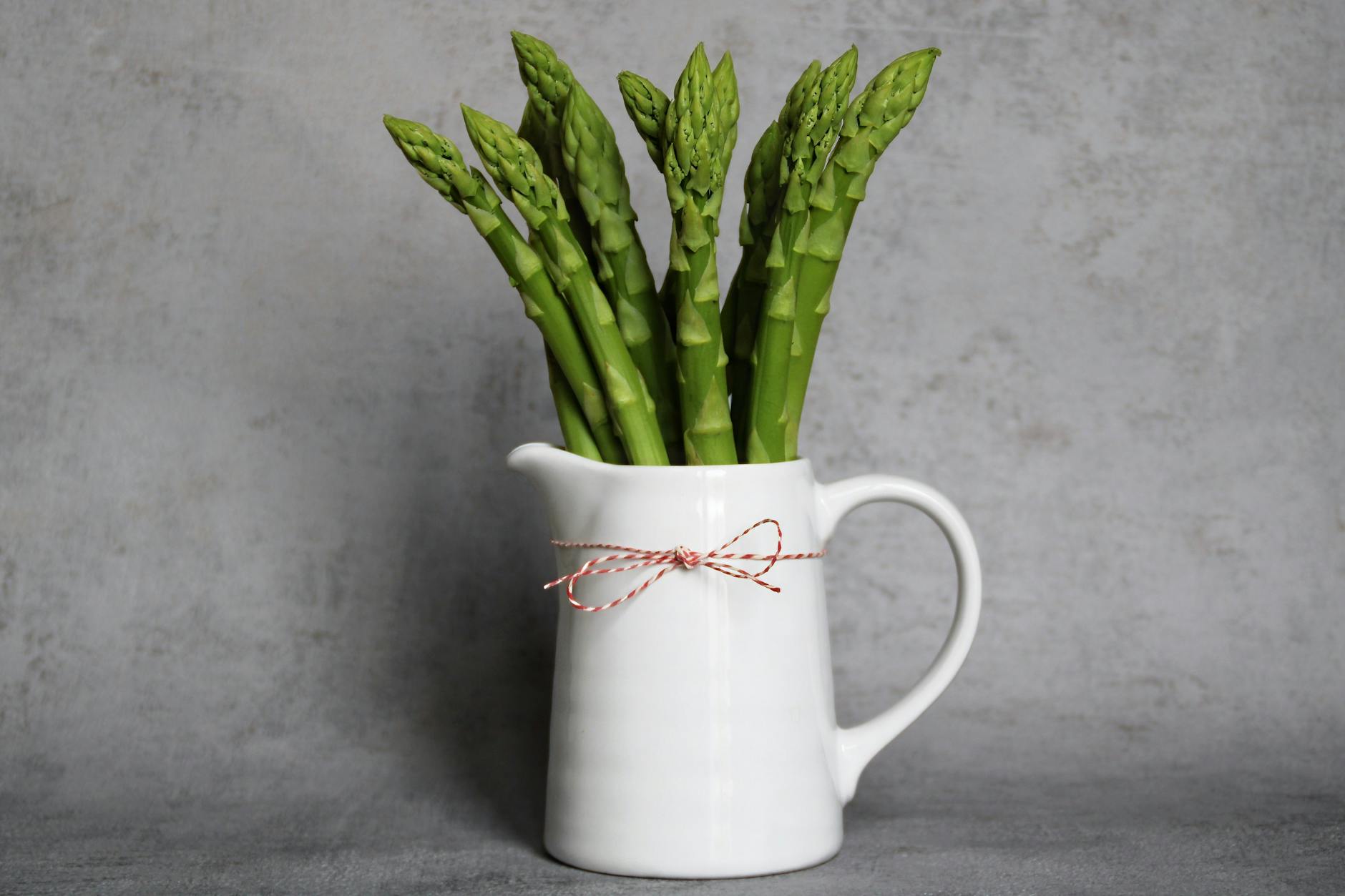 Vibrant green asparagus in a white vase against a textured gray background. - iron rich foods