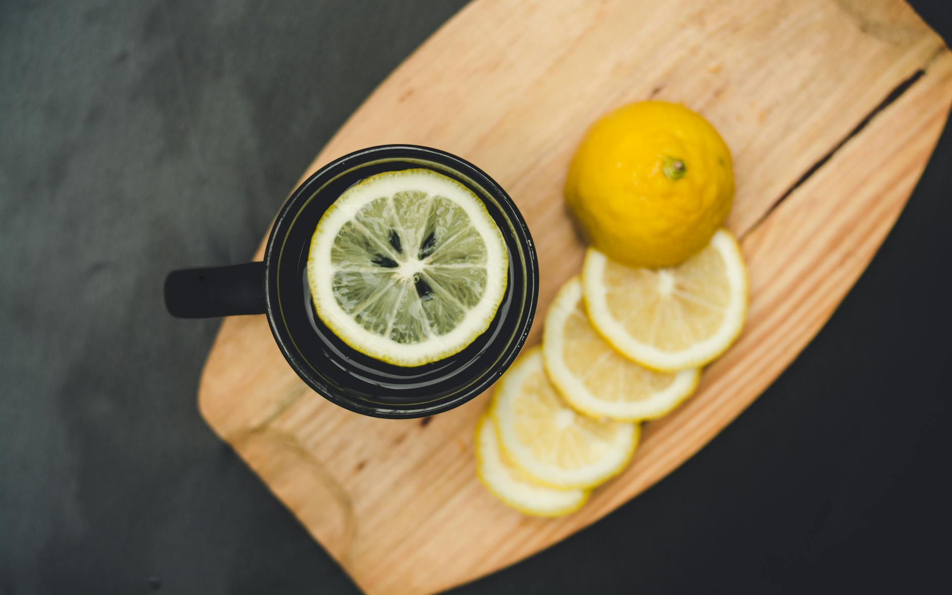 Top view of a black mug with lemon water and sliced citrus on a wooden board. - lemon water benefits