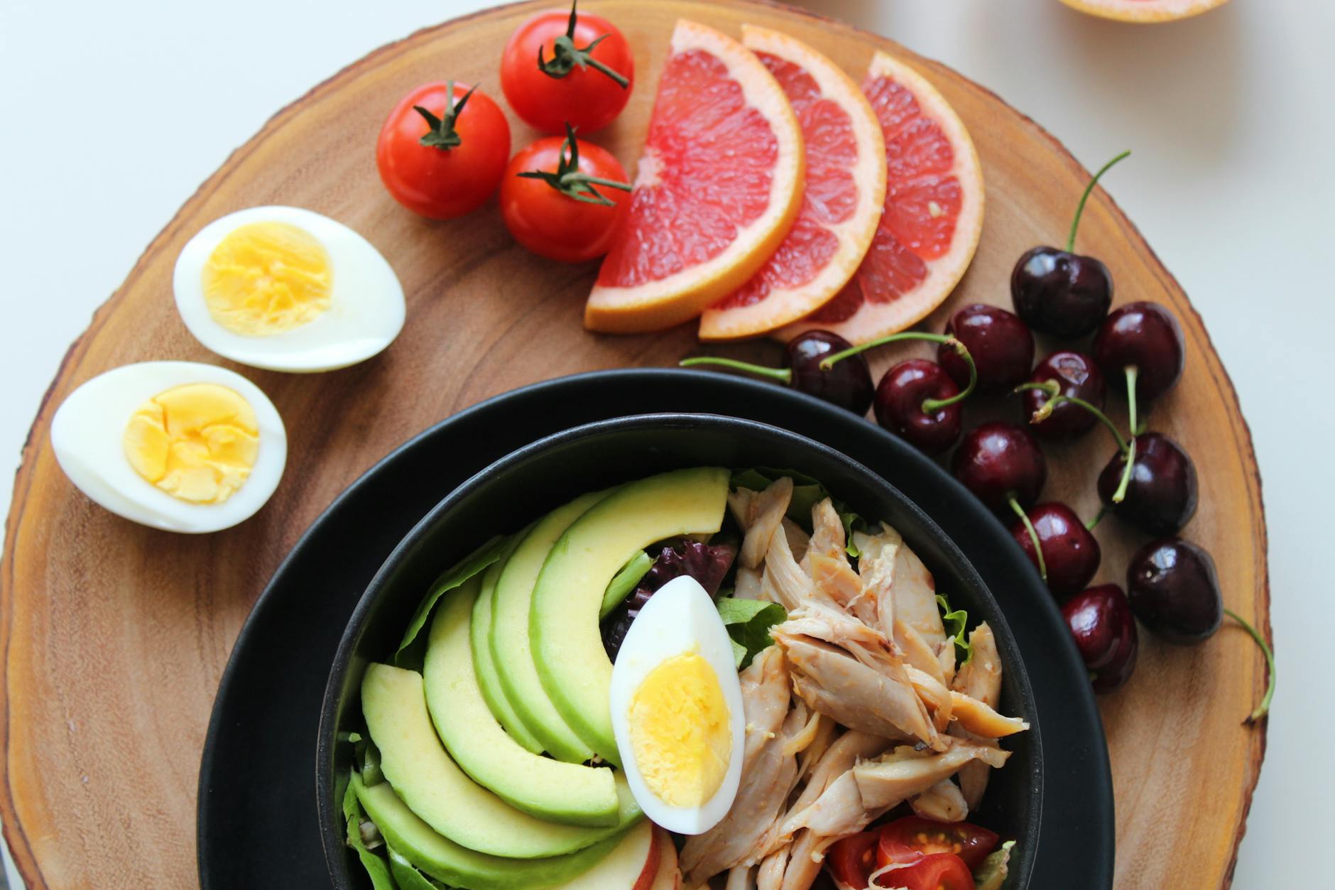 A vibrant, healthy salad bowl with avocado, eggs, tomatoes, grapefruit, and cherries on a wooden board. - low carb diet