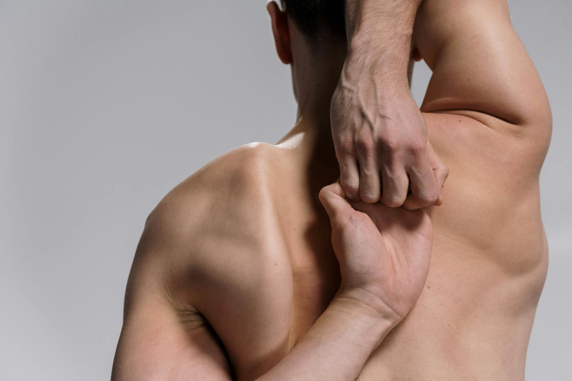 Shirtless muscular man practicing a yoga stretch with hands clasped behind back on a white background. - lower back flexibility exercises