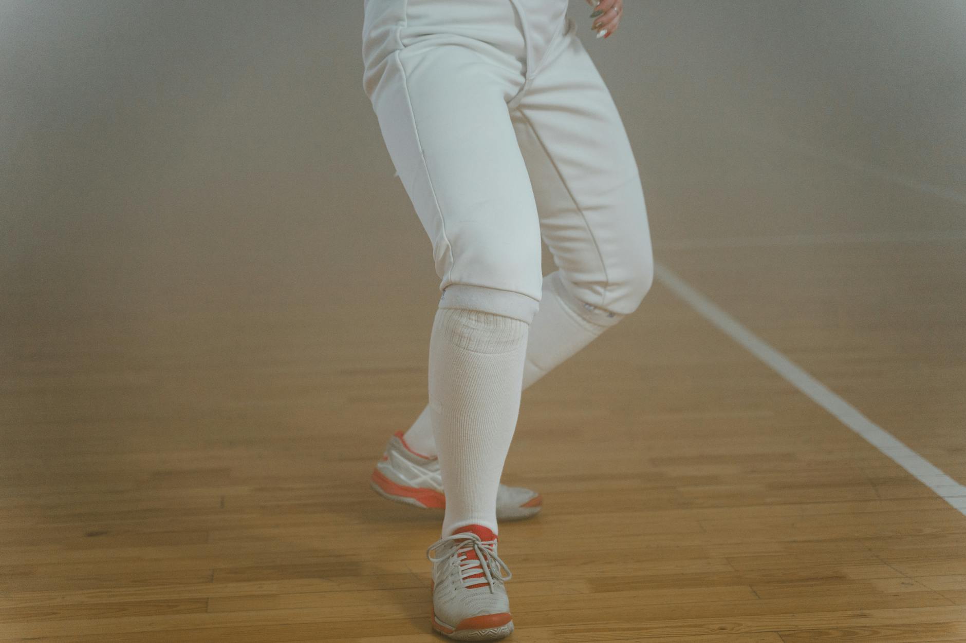 Close-up of a fencer in action, showcasing dynamic movement in white gear on a polished wooden floor. - lower body exercises