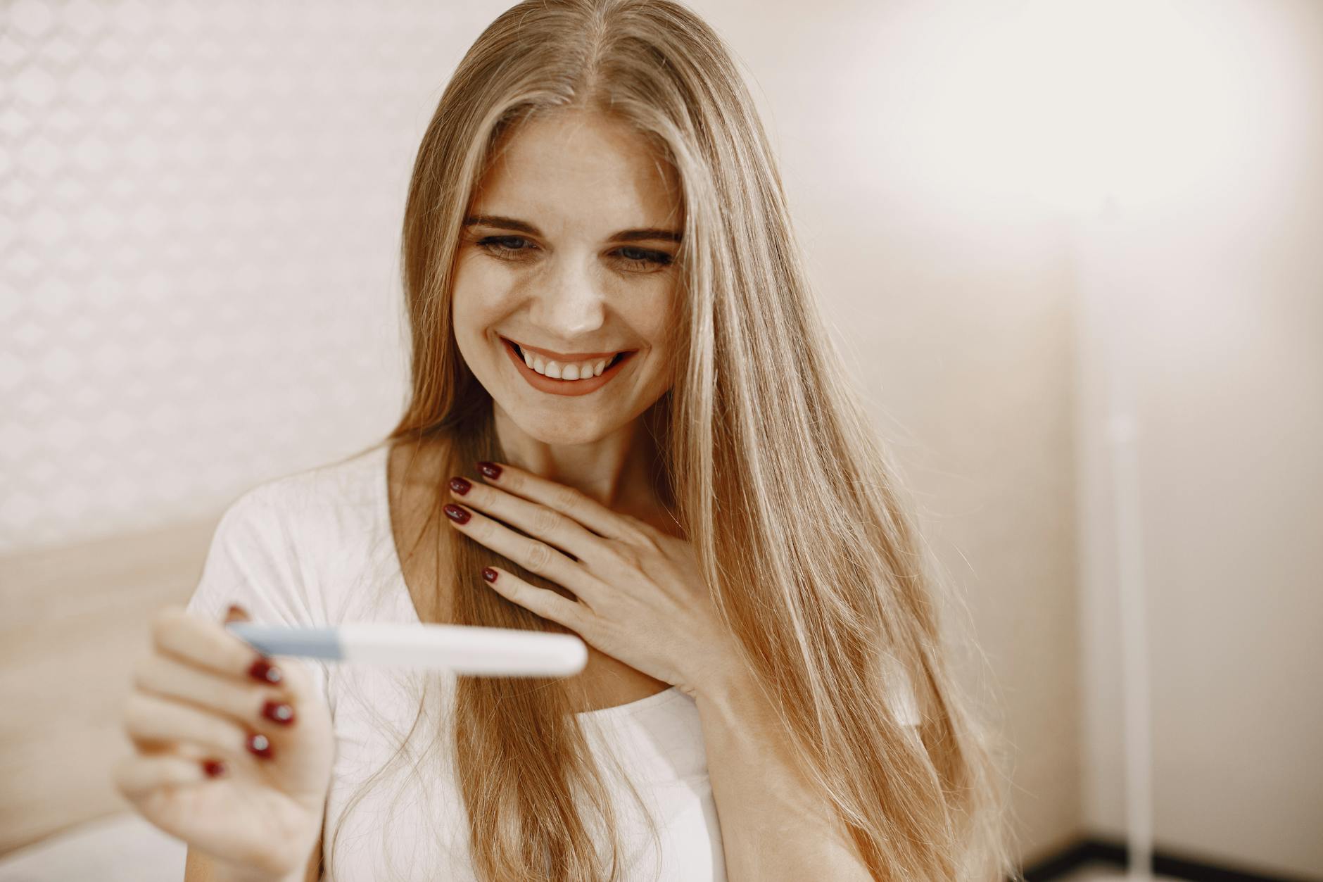 Smiling woman in white with long hair delighted by a positive pregnancy test result indoors. - magnesium glycinate benefits