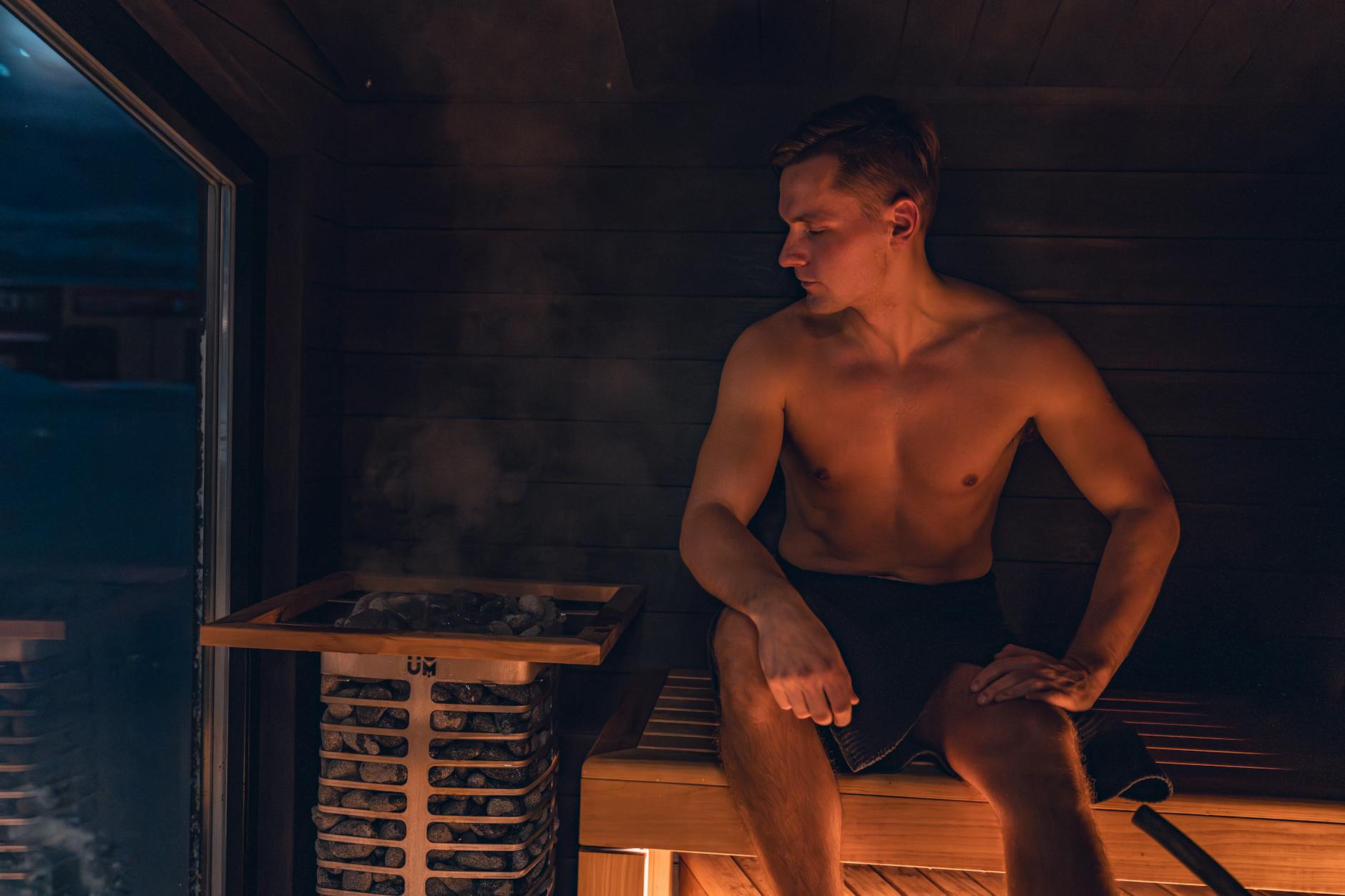 A shirtless man relaxes in a modern Nordic sauna, experiencing the warmth and benefits of steam. - magnesium glycinate benefits