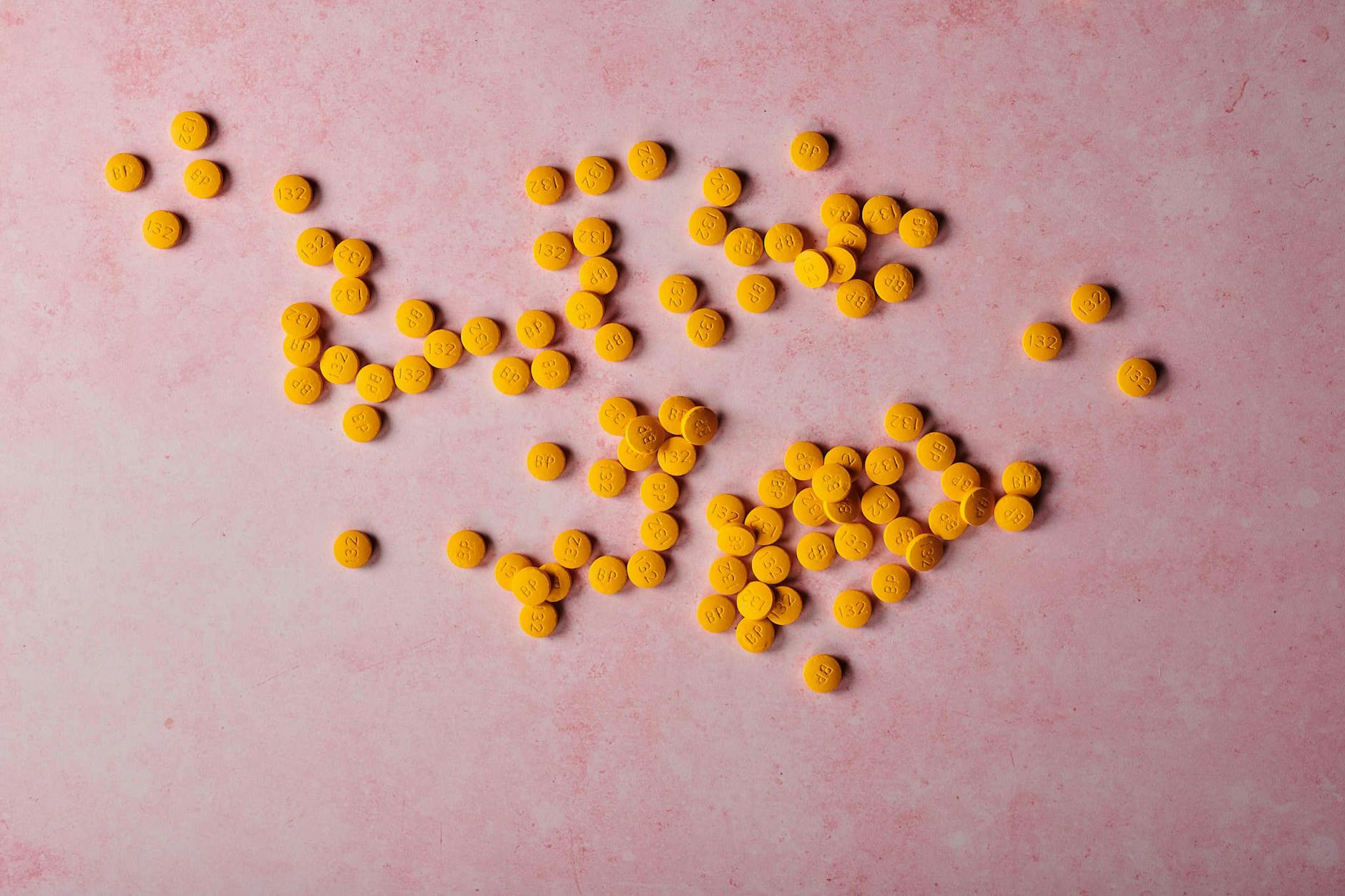Flat lay of yellow pills scattered on a pink surface, ideal for healthcare themes. - magnesium glycinate benefits