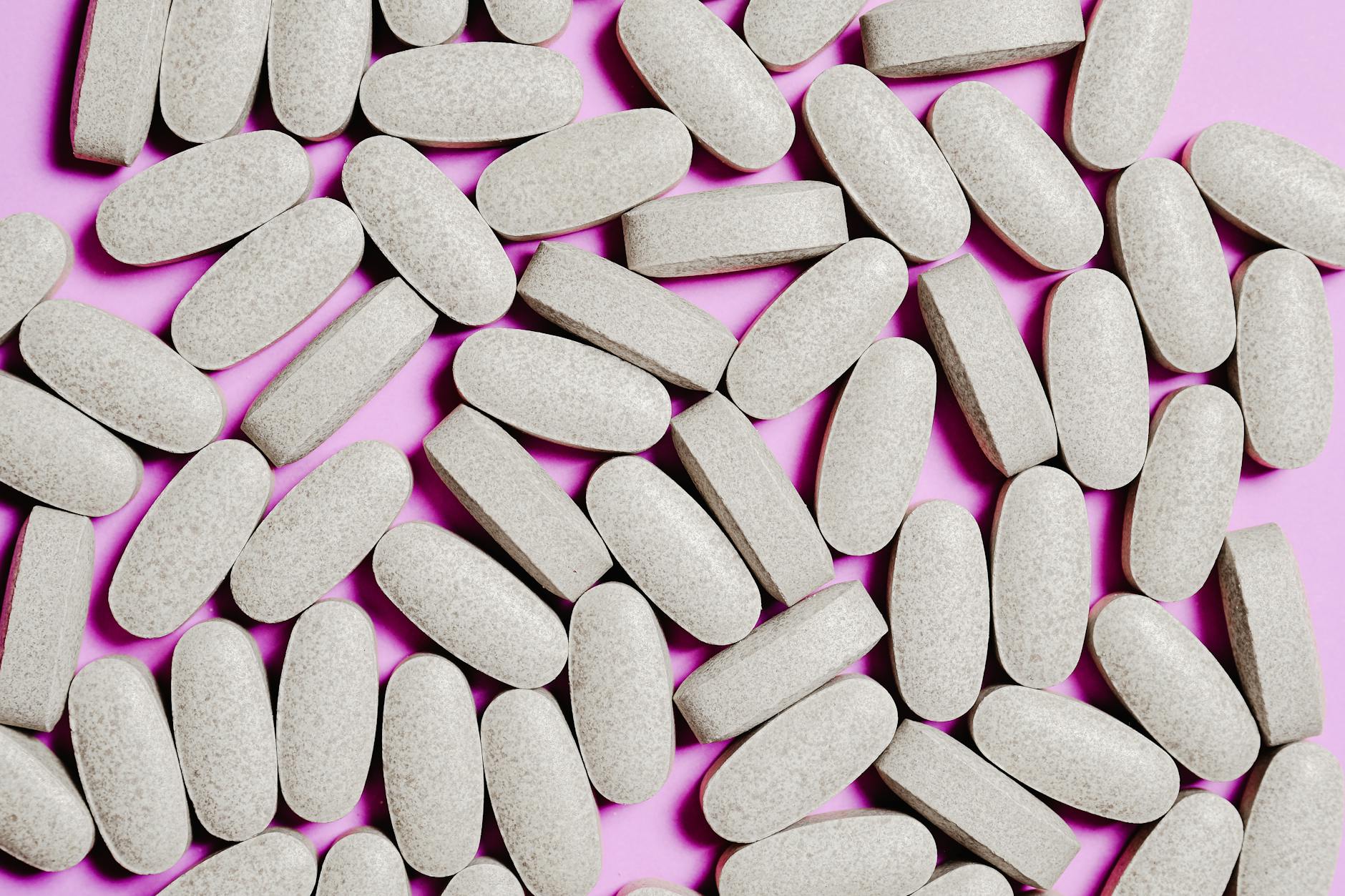 A close-up view of oval tablets scattered on a purple surface. Ideal for healthcare and pharmaceutical concepts. - magnesium supplement benefits