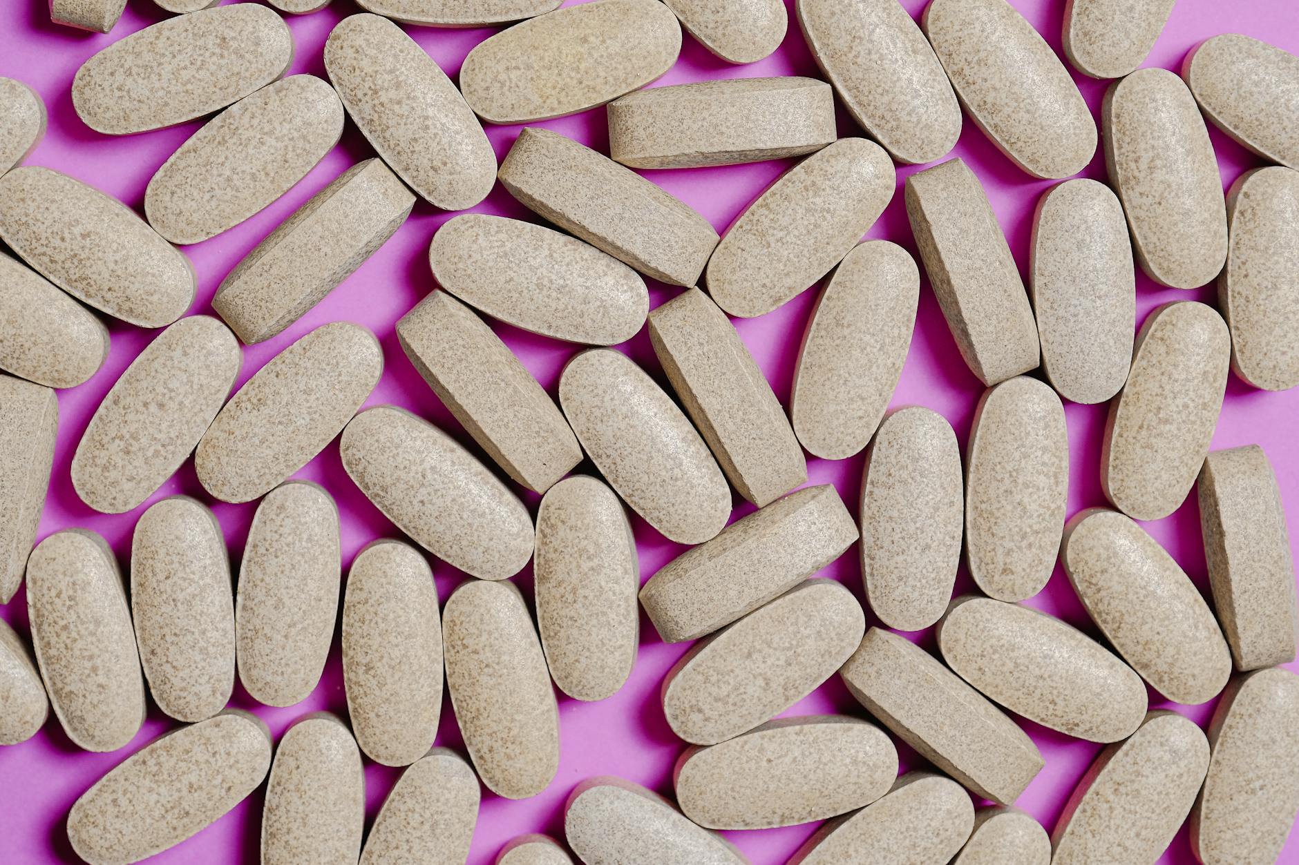 Brown oblong tablets scattered on a bright pink background, highlighting healthcare themes. - magnesium supplement benefits
