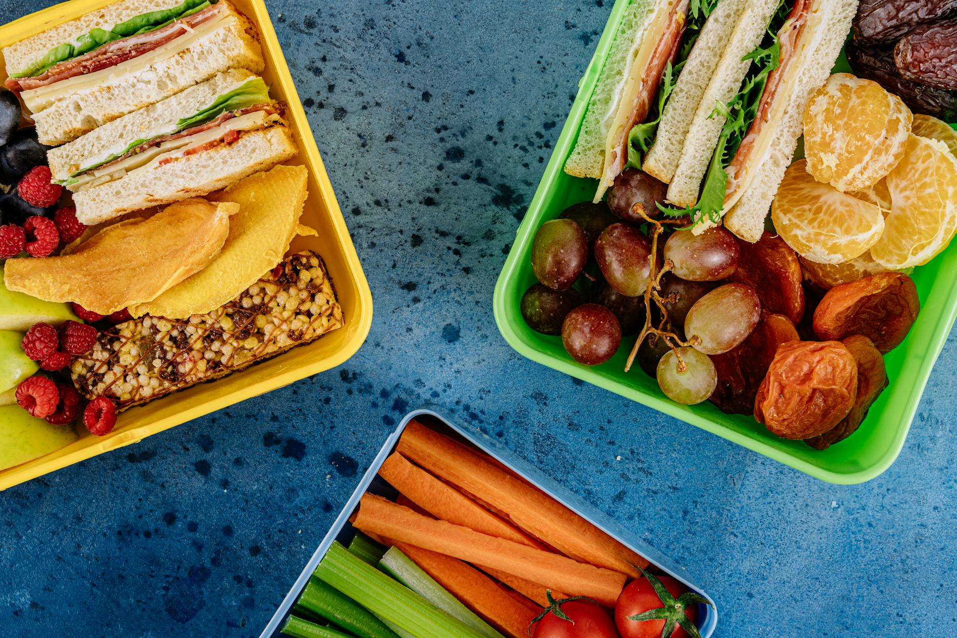 Top view of vibrant lunch boxes filled with sandwiches, fruits, and vegetables on a blue surface. - meal prep ideas
