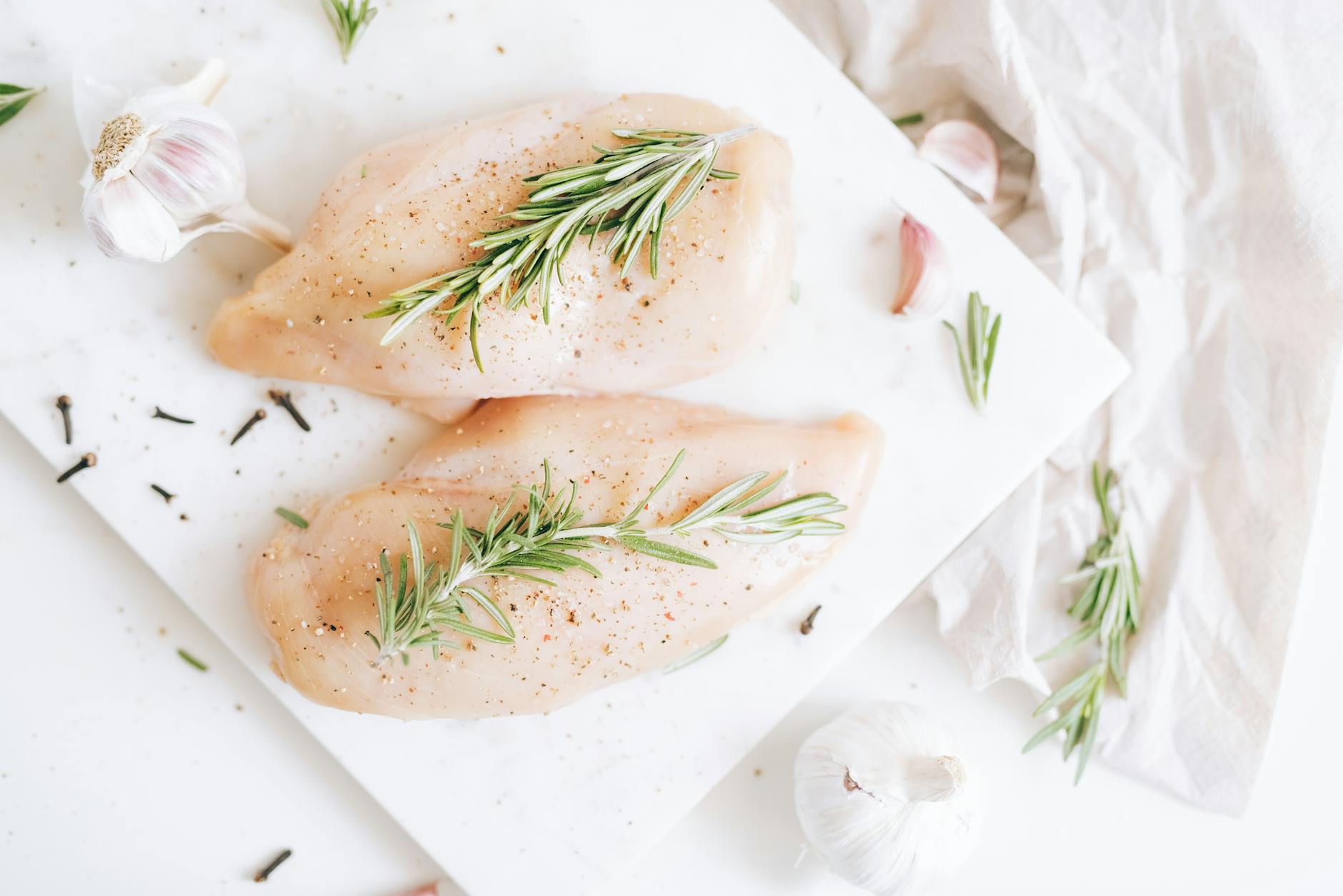 Raw chicken breasts seasoned with rosemary and garlic on a cutting board. - mediterranean chicken recipe