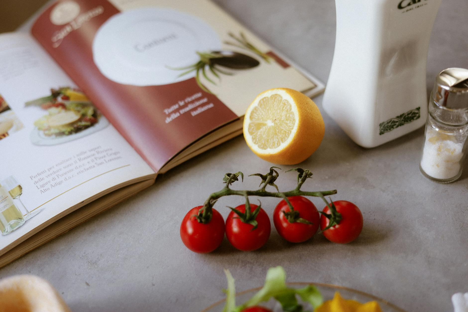 Flat lay of cooking ingredients including tomatoes and a lemon with a cookbook. - mediterranean diet plan