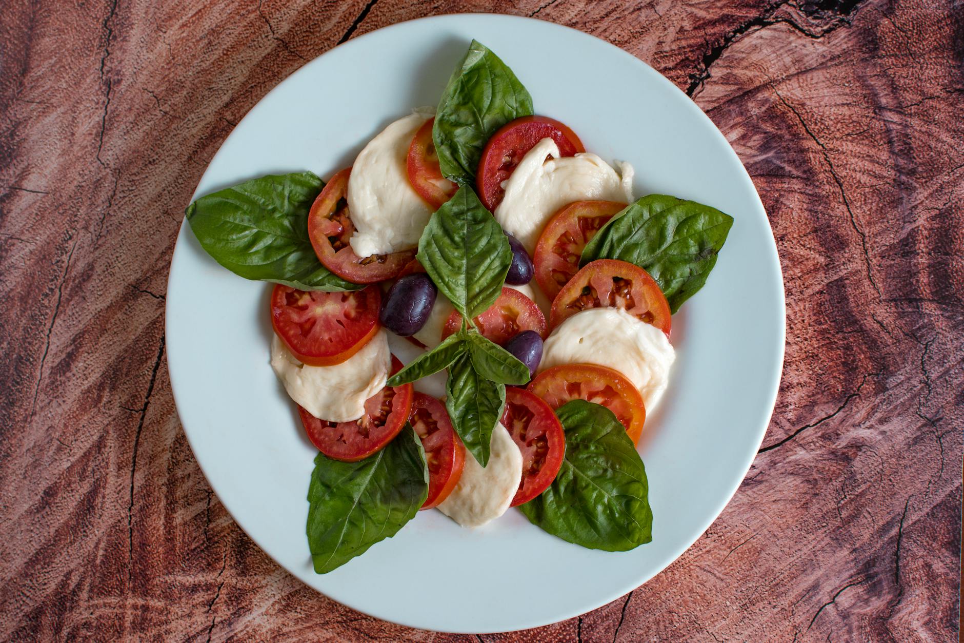 Top view of a fresh Caprese salad featuring tomatoes, mozzarella, basil, and olives. - mediterranean salad recipe
