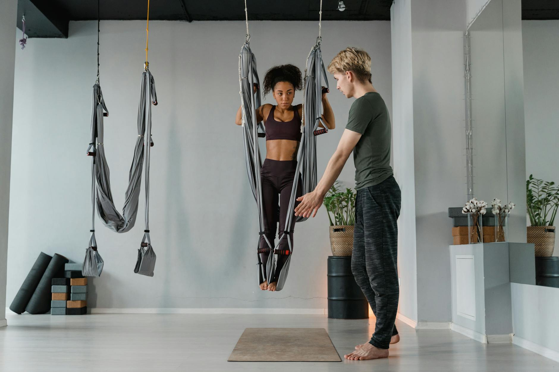 Instructor assists woman practicing aerial yoga in a studio setting with hammocks. - mindful meditation benefits