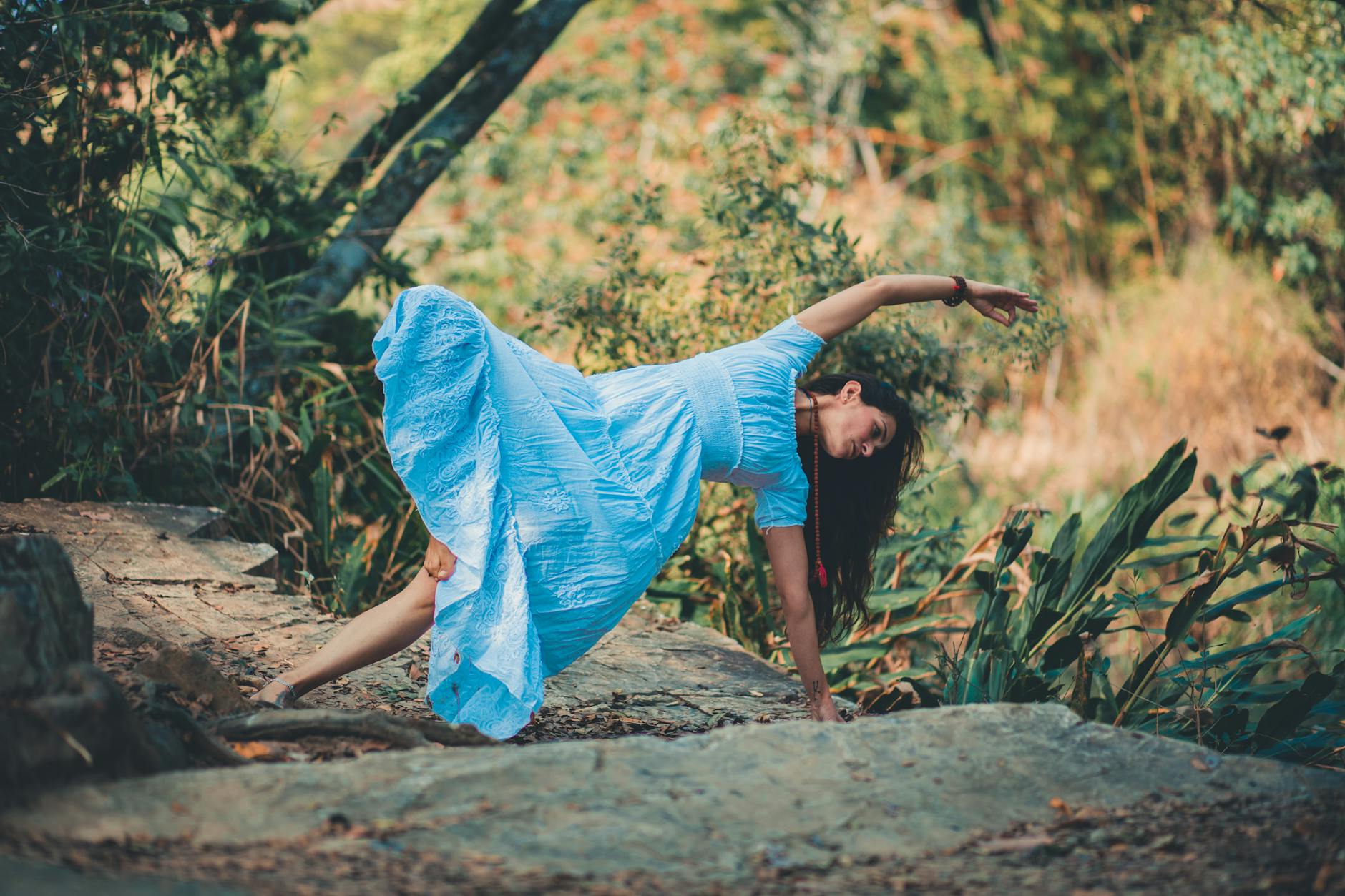 Full body of barefoot female in dress doing lateral bend supported by leg and arm in nature during yoga session - mindful movement