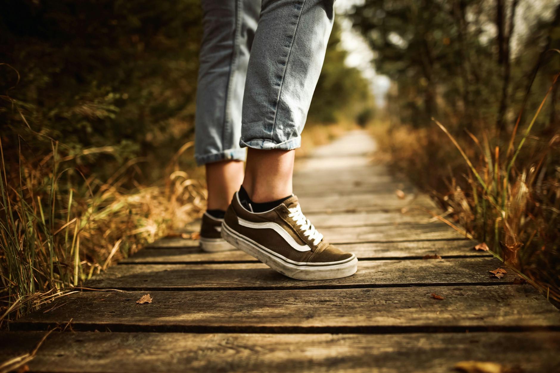 Close-up of a person walking on a wooden path in a park wearing jeans and sneakers during autumn. - mindful nature walks
