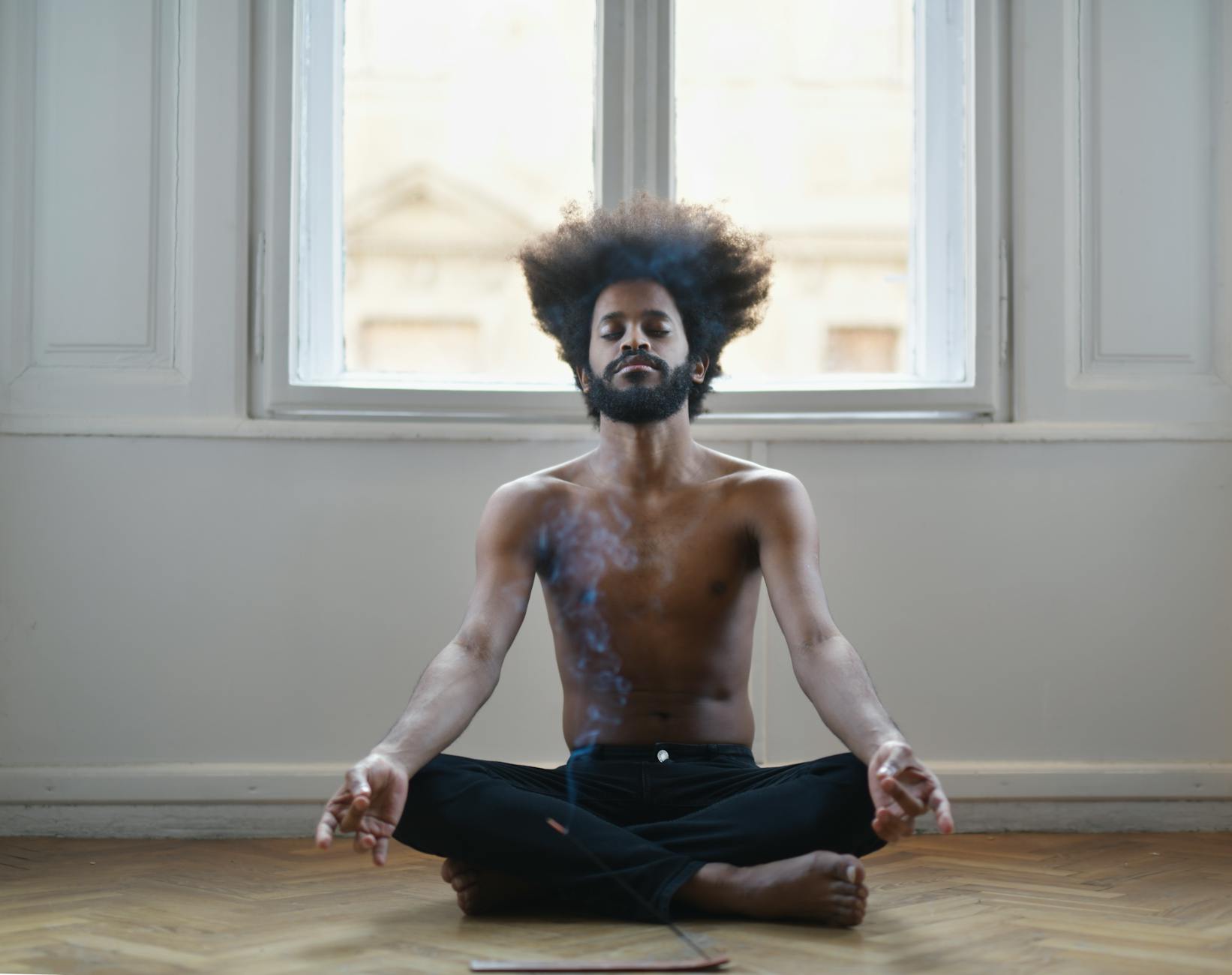 Shirtless man meditating on the floor, surrounded by soothing incense smoke in a tranquil room. - mindfulness meditation benefits