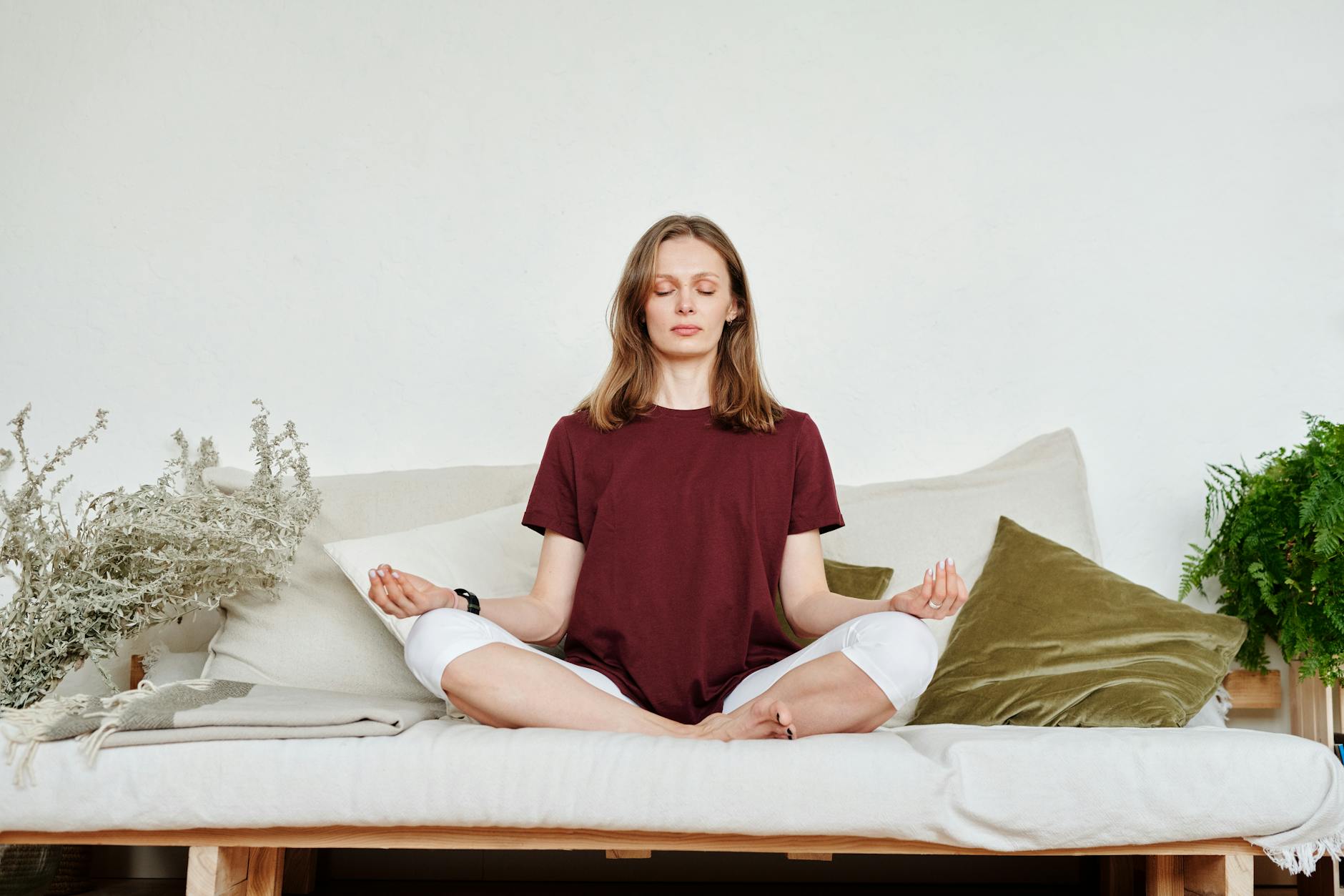 Woman meditating indoors on a sofa, exuding calmness and mindfulness, surrounded by greenery. - mindfulness for sleep