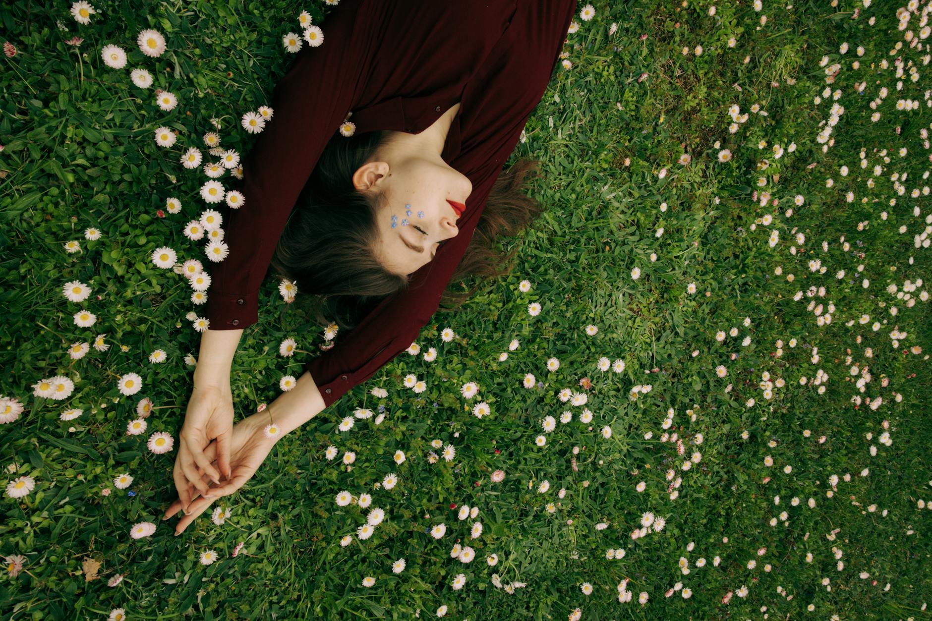 Woman lying peacefully on a grassy field with daisies, embodying relaxation and nature connection. - mindfulness for sleep