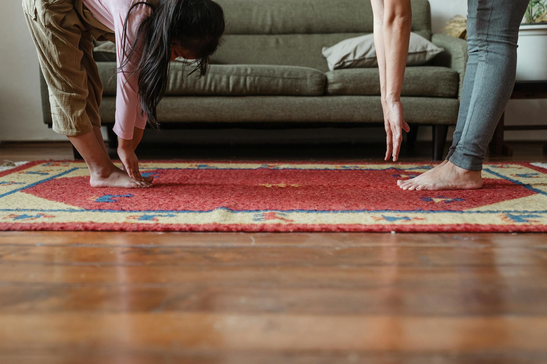 Side view of young ethnic woman stretching body with adorable girl while standing against each other on floor carpet near cozy sofa in modern living room in morning - morning exercise kids