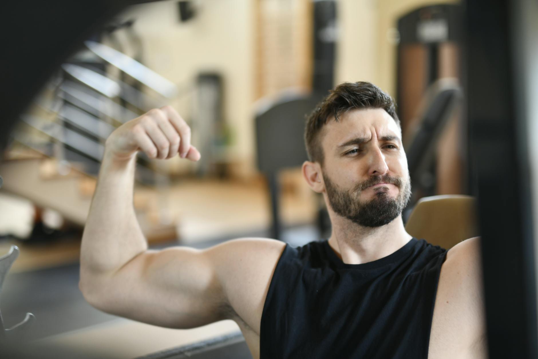 A bearded man confidently flexing his arm muscles inside a gym, showcasing strength and fitness. - morning muscle activation