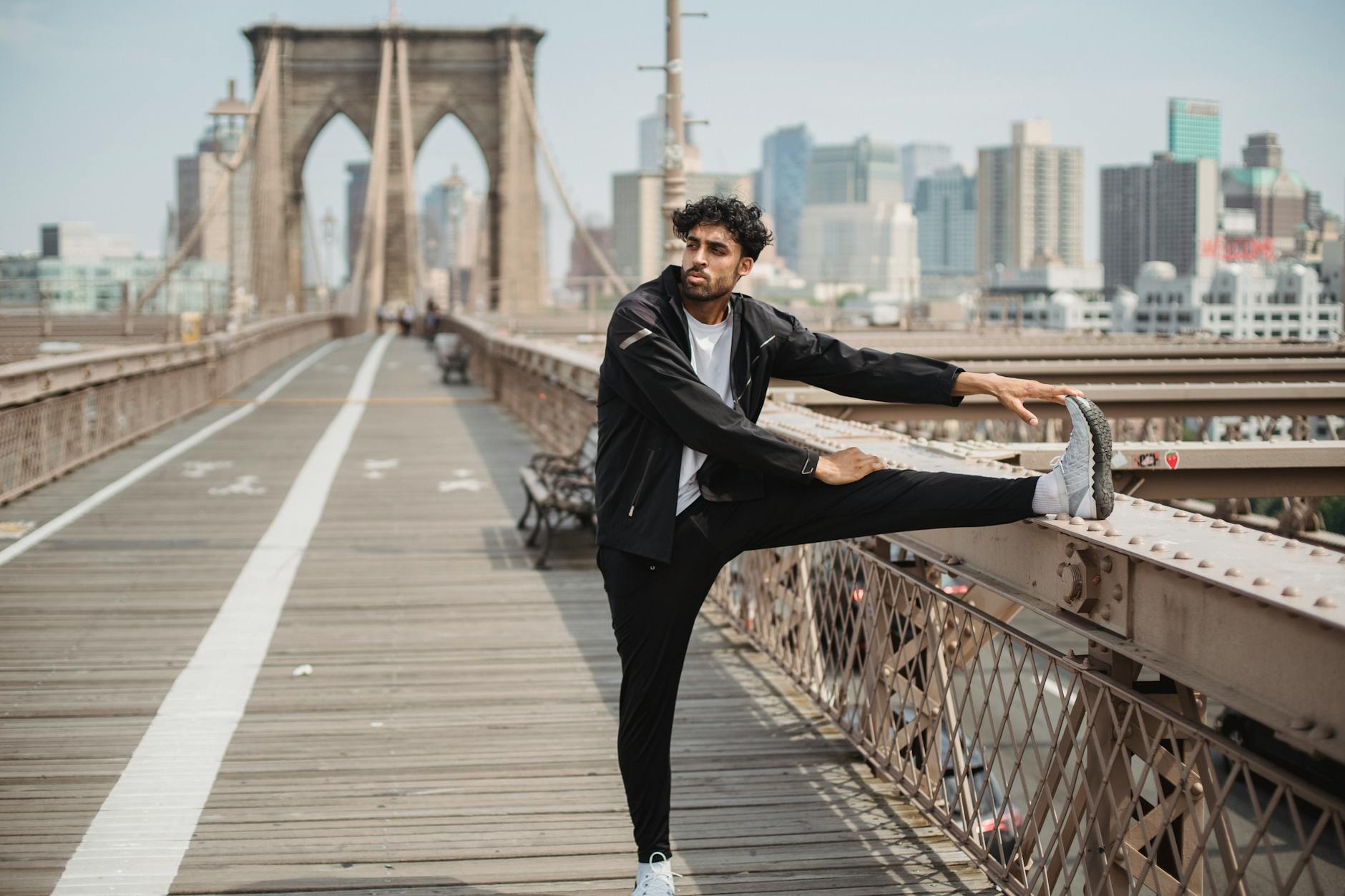 Adult man performs stretching exercises on the Brooklyn Bridge with a city skyline in the background. - morning stretch routine