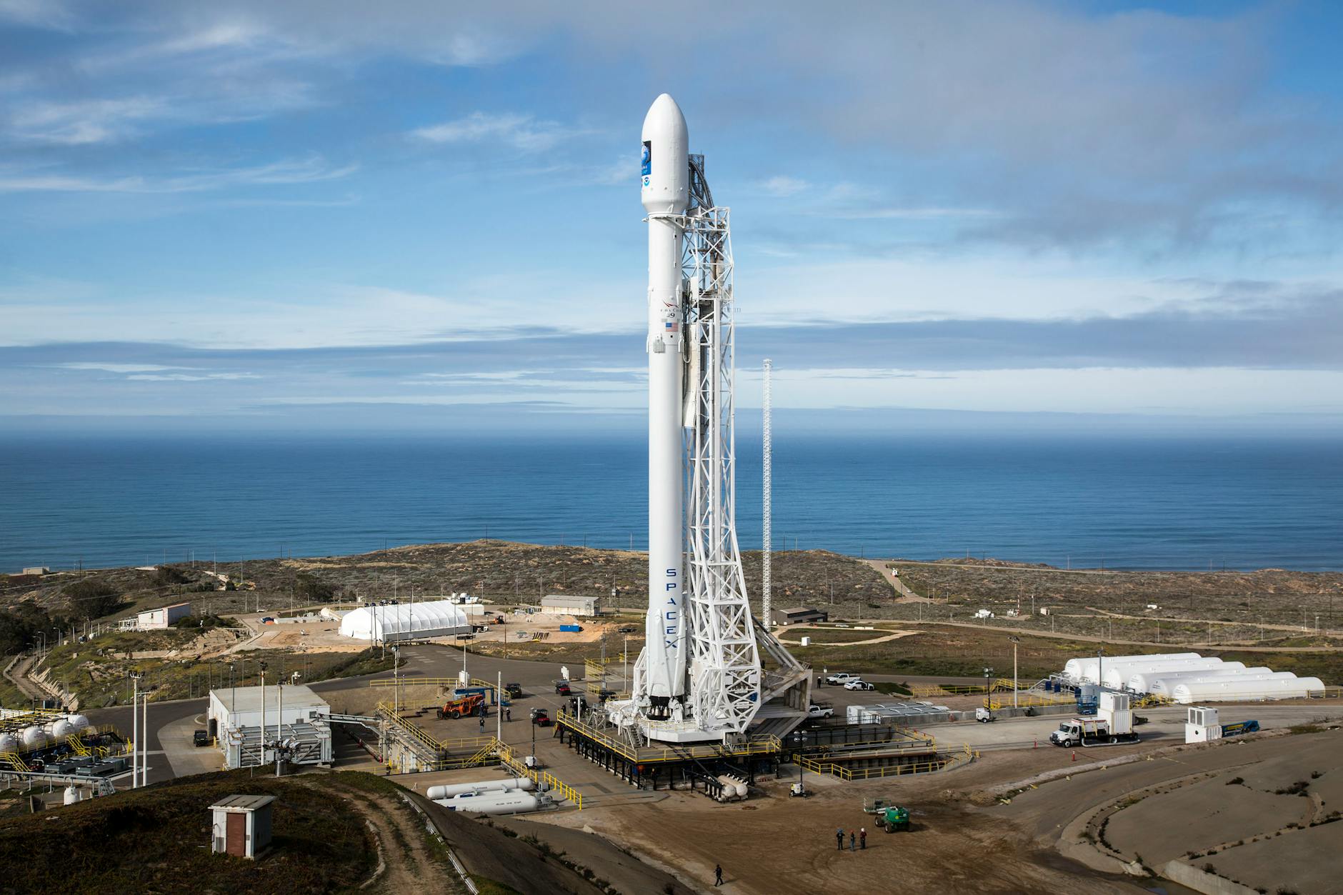 A SpaceX rocket stands on a launch pad overlooking the ocean under a clear sky. - natural energy boosters