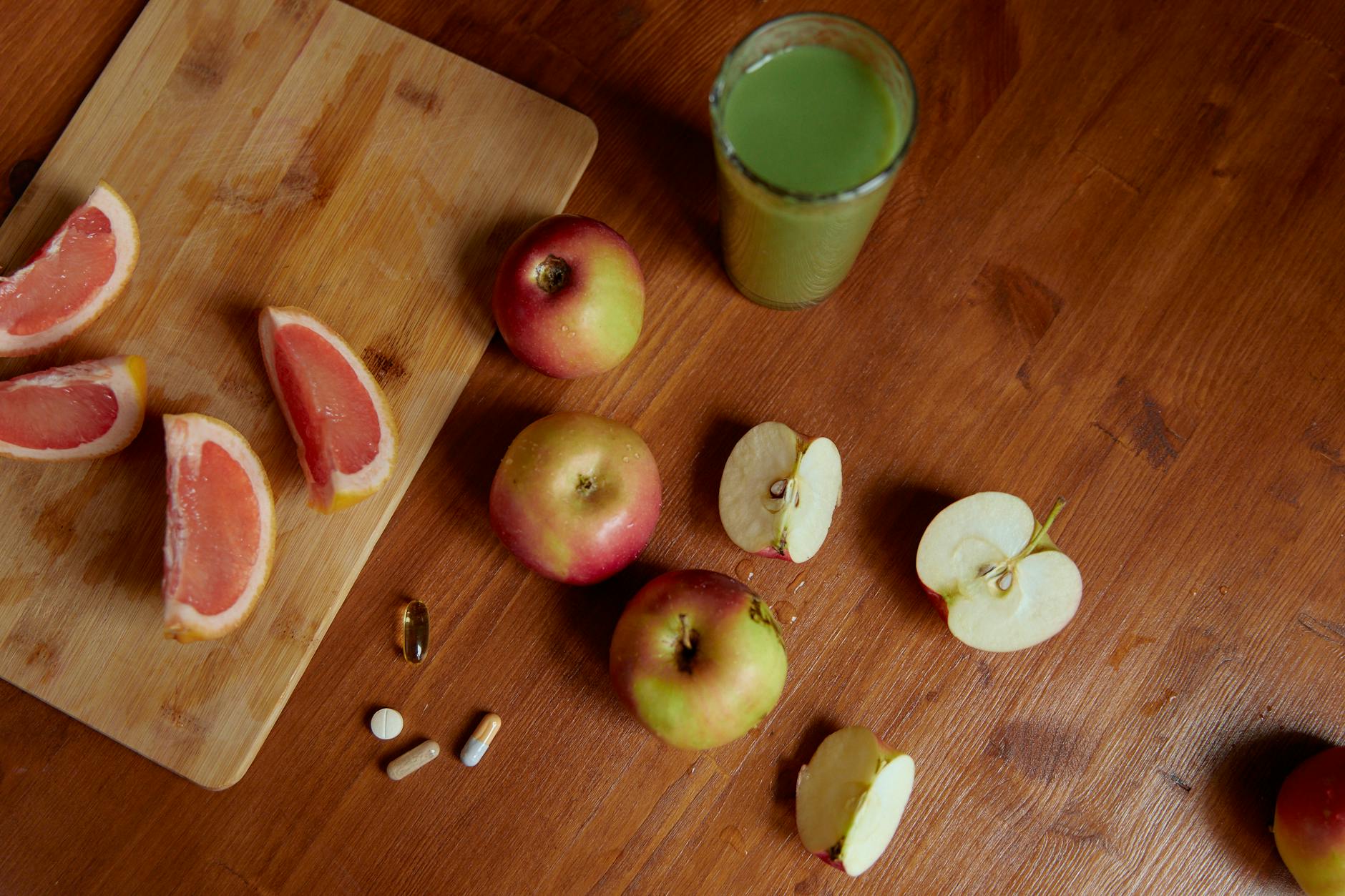 Top view of sliced grapefruit, apples, pills, and a green drink on a wooden table, emphasizing health. - natural immune support