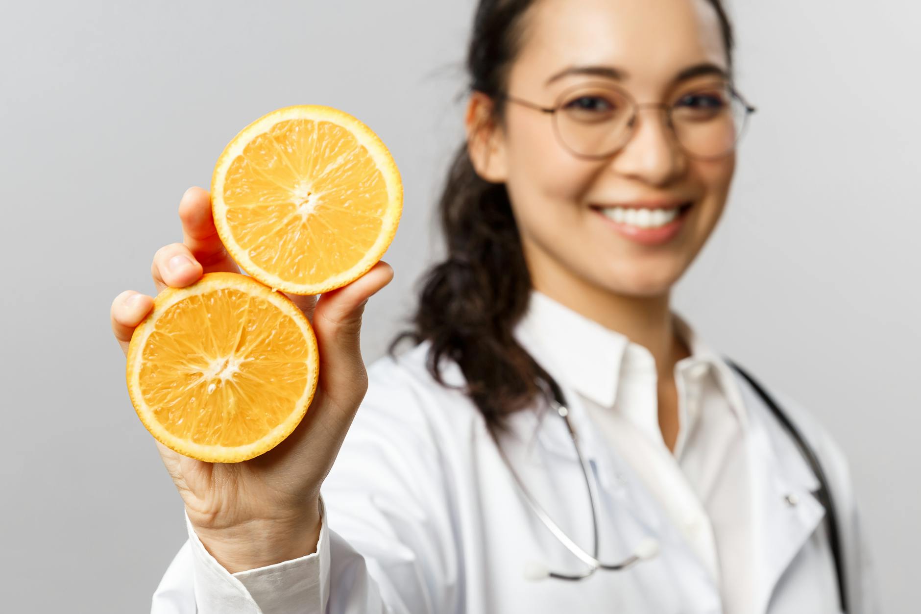 Cheerful female doctor with glasses presenting two halves of a sliced orange, promoting health. - natural immune support