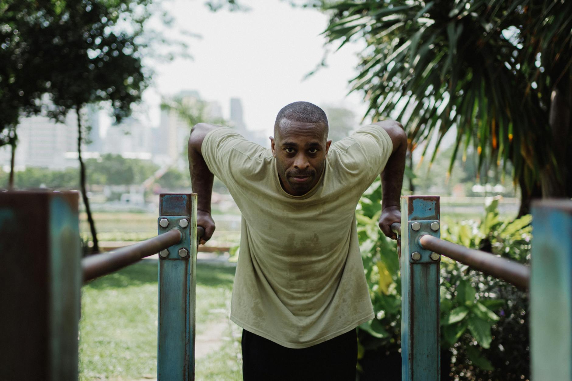 Man exercising outdoors using parallel bars in a park setting. Focus on strength and fitness. - neck posture exercises