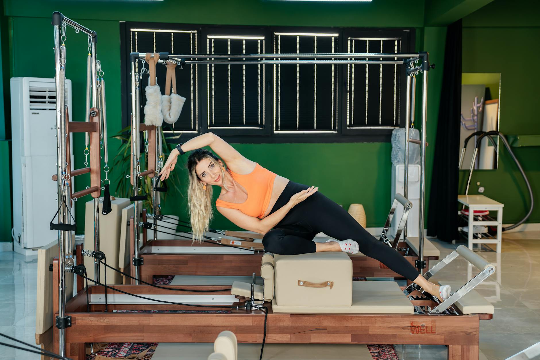 Woman performing side stretch exercise on Pilates reformer machine indoors. - pilates reformer exercises