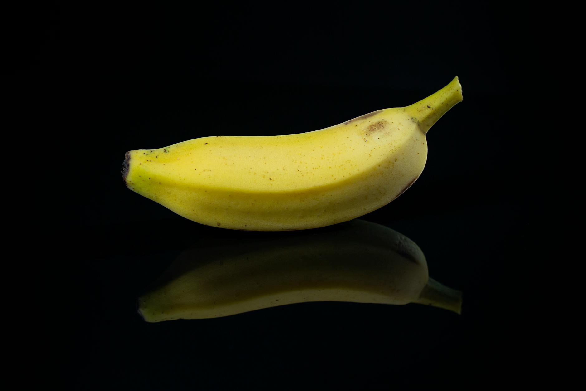 Close-up of a single banana reflecting on a glossy black surface. - potassium rich foods