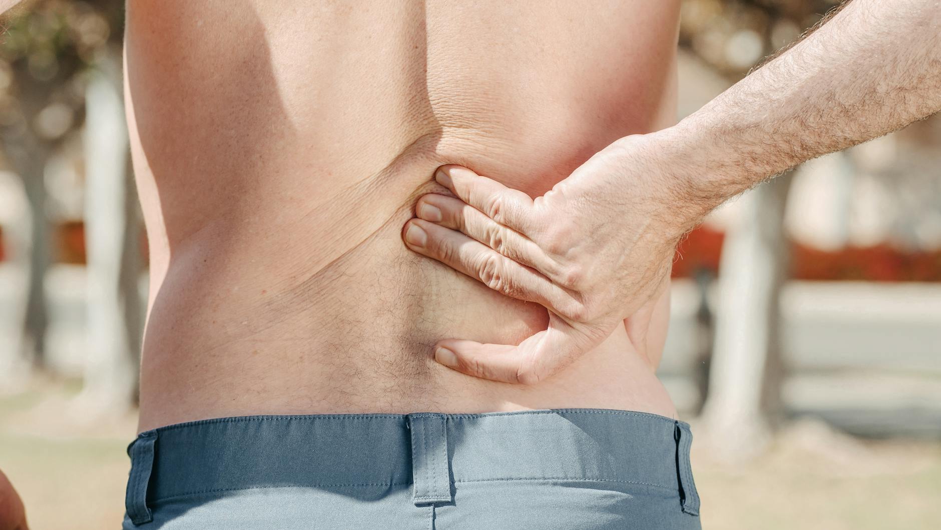 Close-up of a man holding his lower back in pain, possibly indicating discomfort or injury. - pregnant back pain