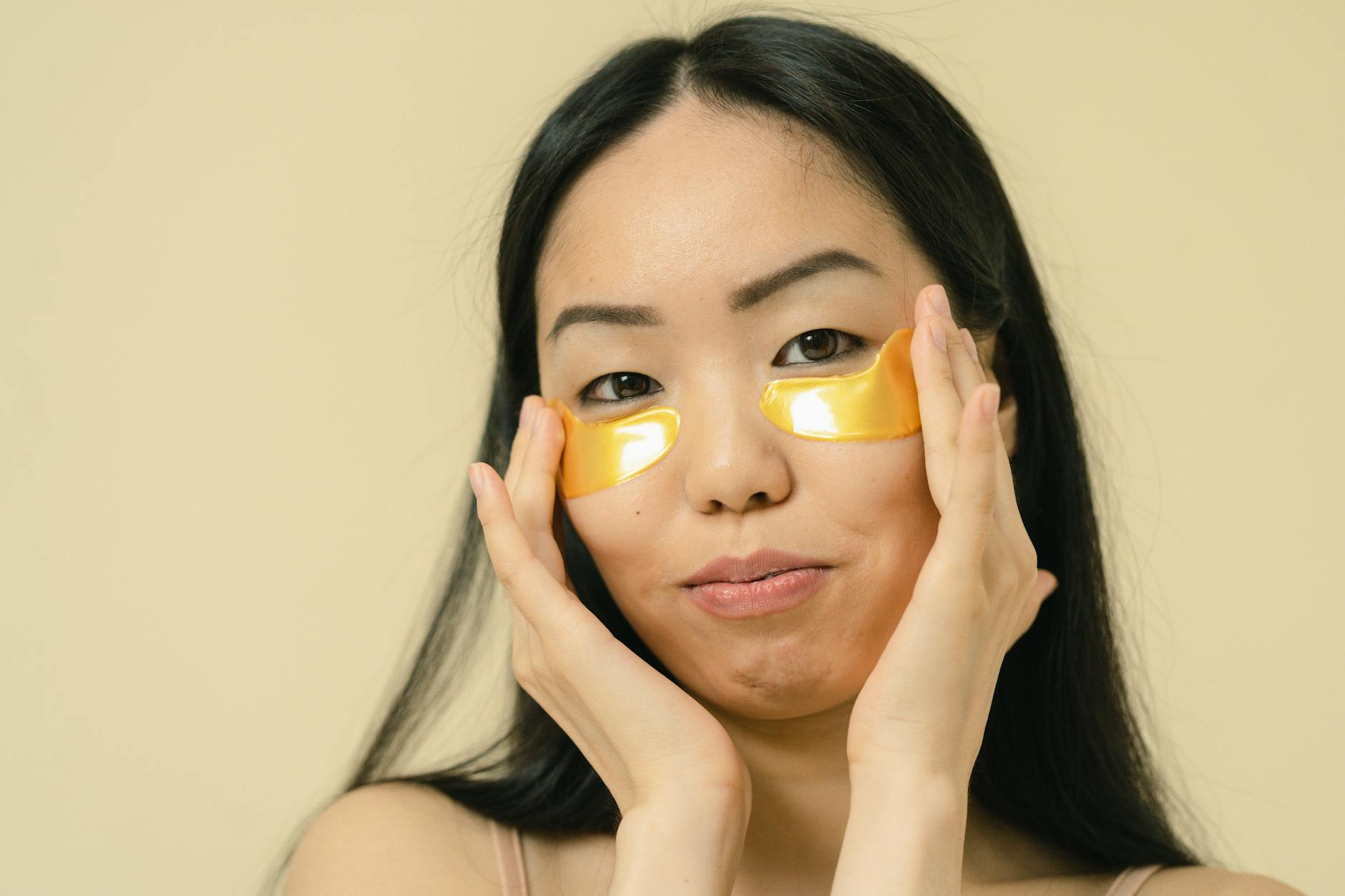Woman with long black hair using gold eye patches for skincare in a studio. - radiant skin foods