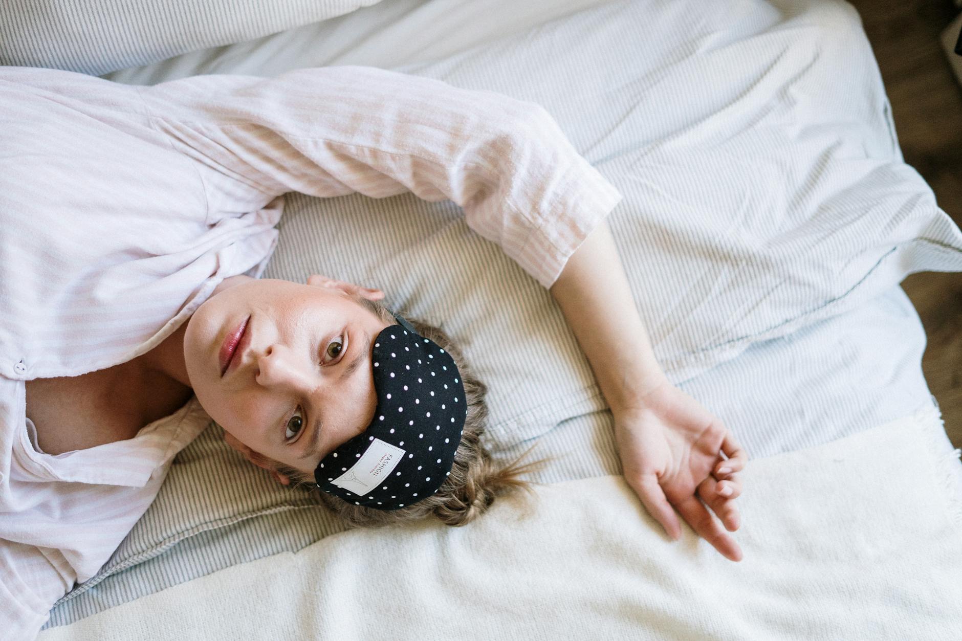 A young woman wears a polka dot eye mask while lying comfortably in bed during the day. - seated good morning